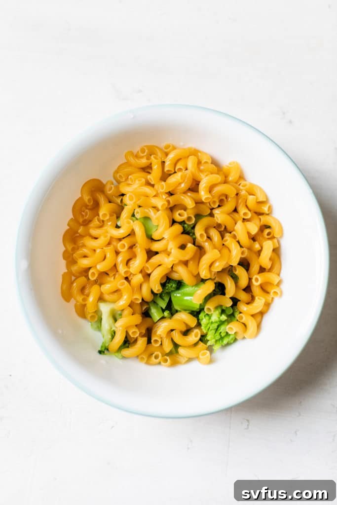 A microwave-safe bowl filled with uncooked pasta, frozen broccoli, and water, ready for cooking.