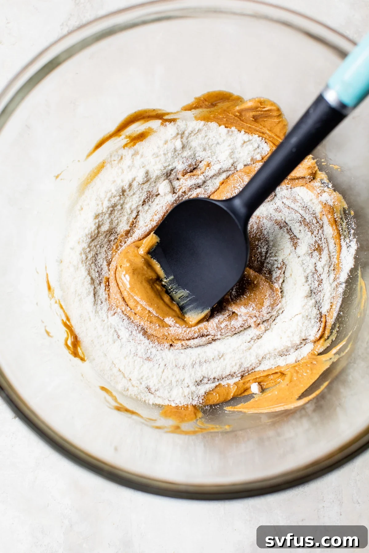 A glass bowl containing a creamy mixture of peanut butter and coconut flour, ready to be formed into delicious balls.