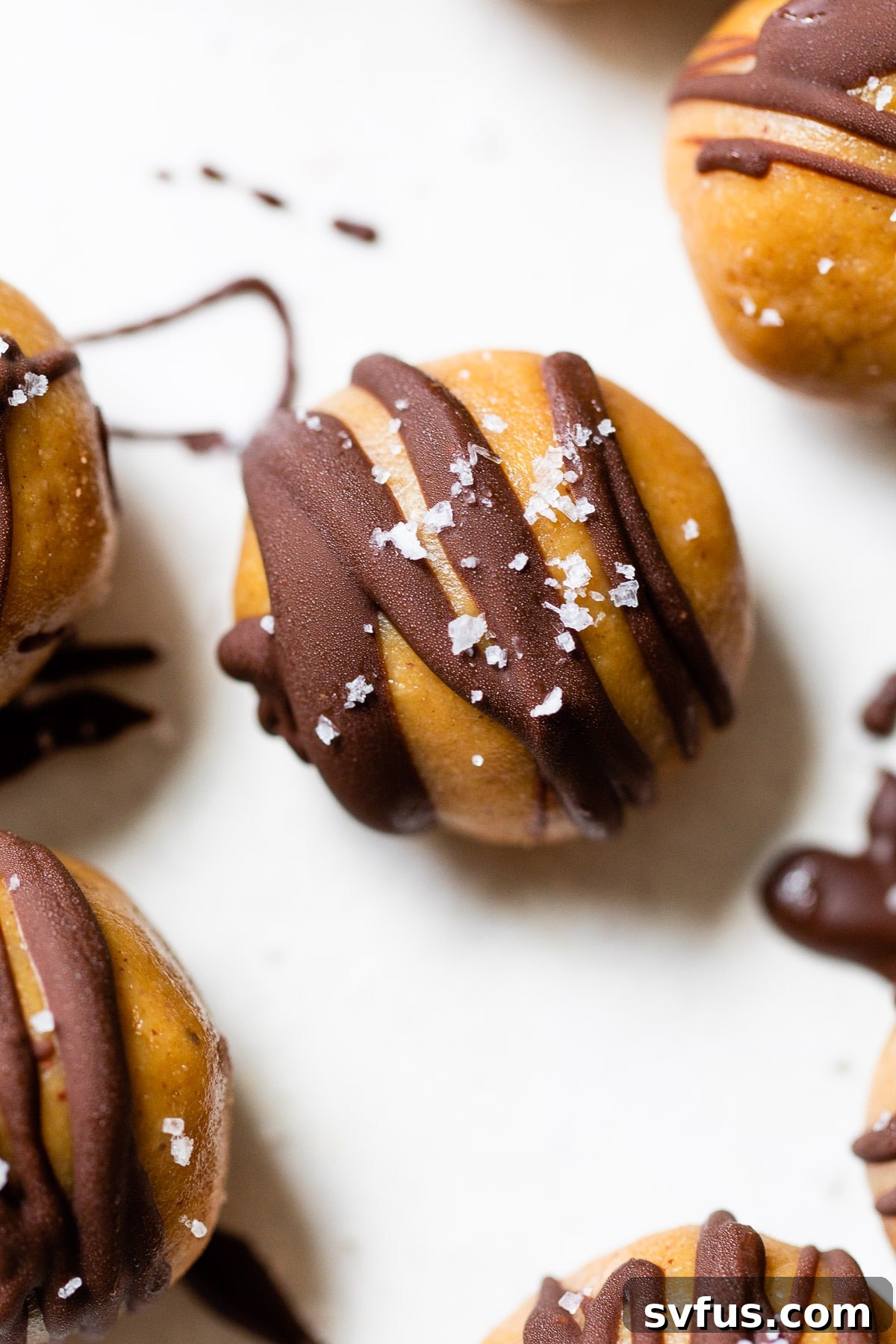 A close-up of a single healthy peanut butter ball, beautifully drizzled with chocolate and garnished with sea salt, highlighting its enticing texture.