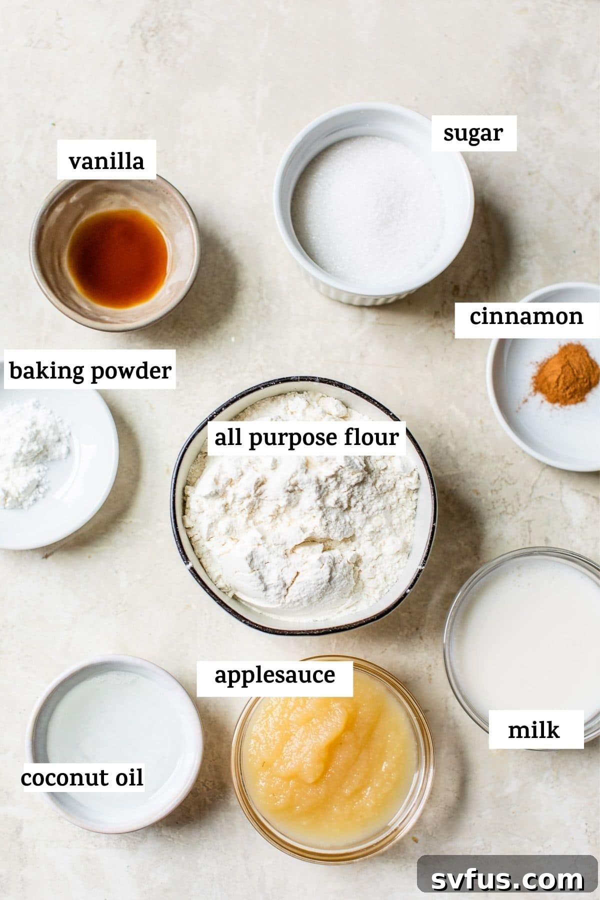 Assorted vegan donut ingredients laid out on a kitchen counter, including flour, sugar, milk, and applesauce.