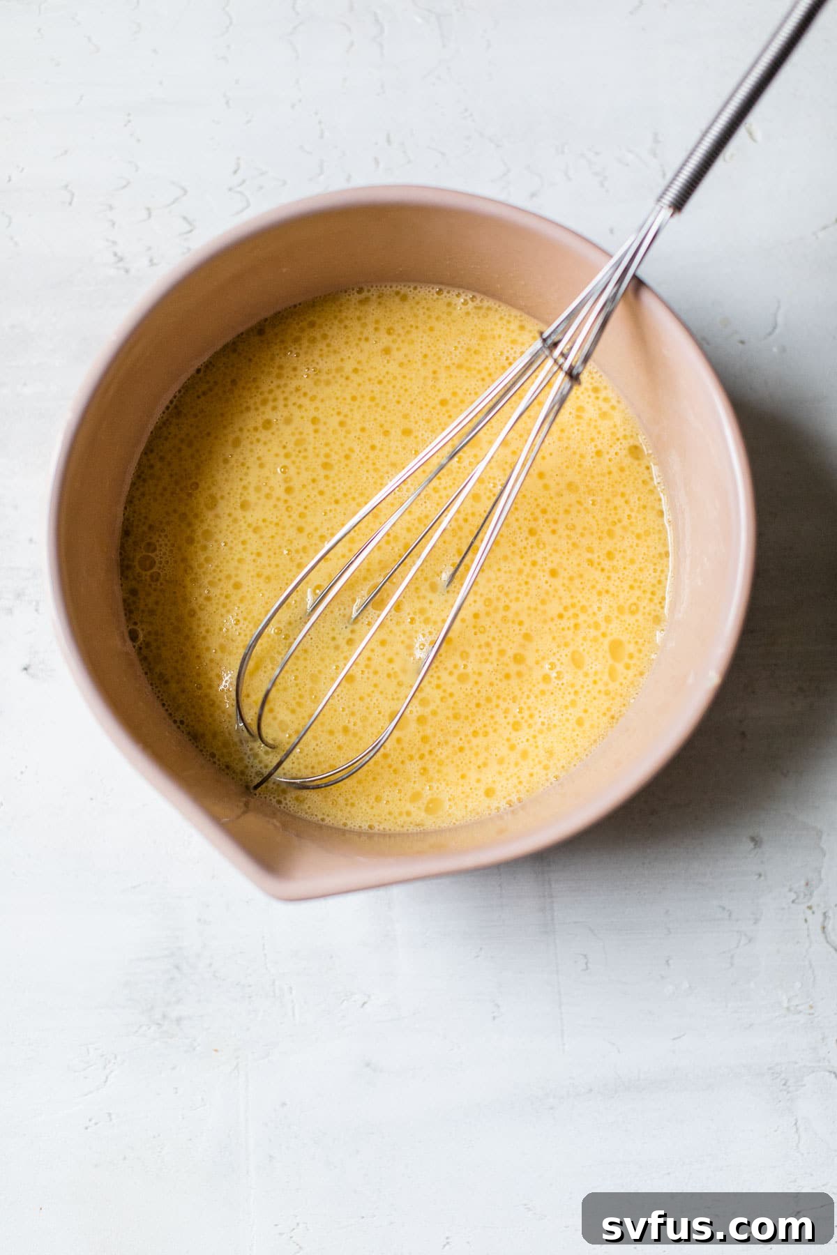 Wet ingredients (eggs, almond milk, maple syrup, cooled coconut oil) being whisked together in a glass bowl.