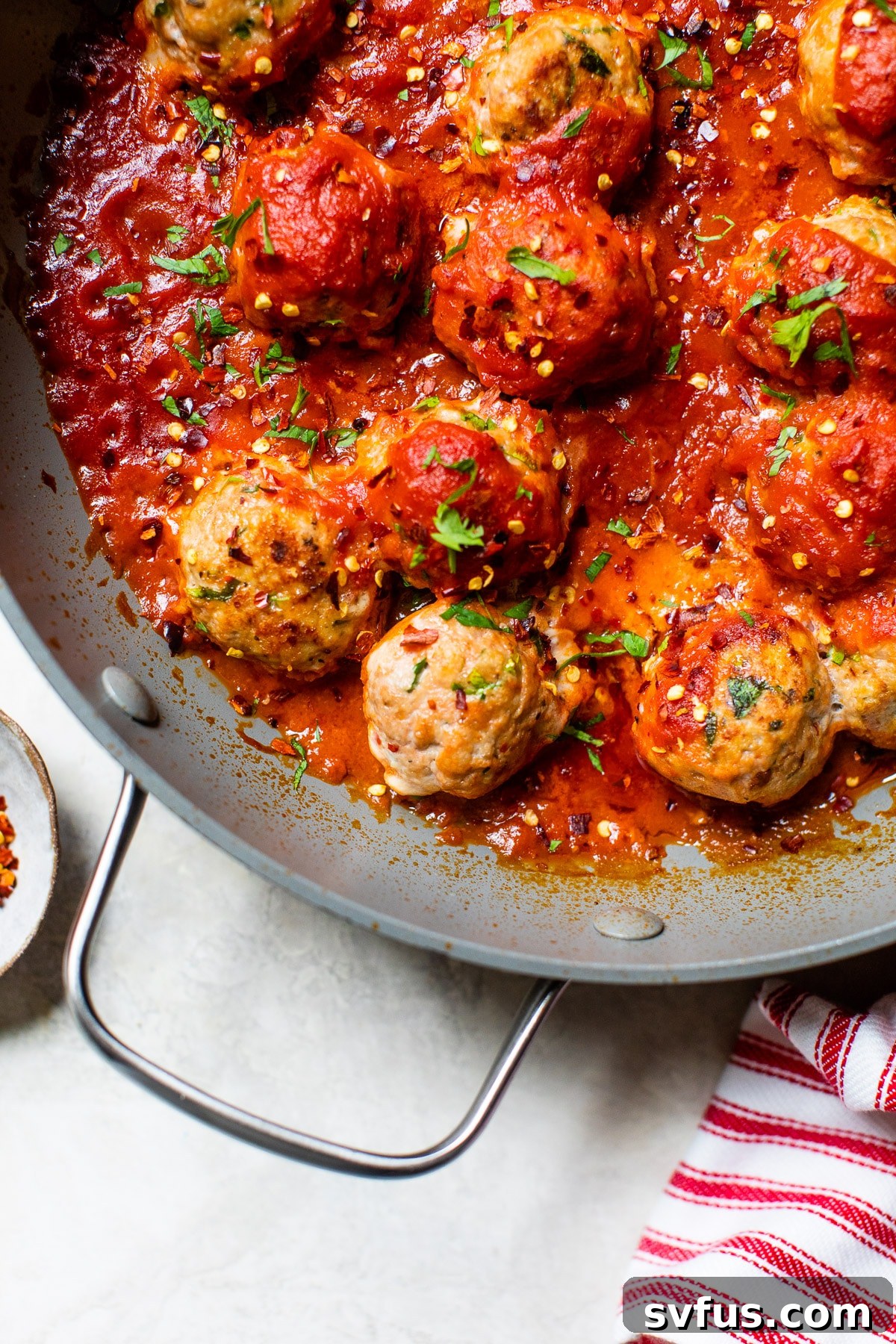Close-up shot of seared paleo turkey meatballs covered in red sauce, glistening in an oven-safe skillet.