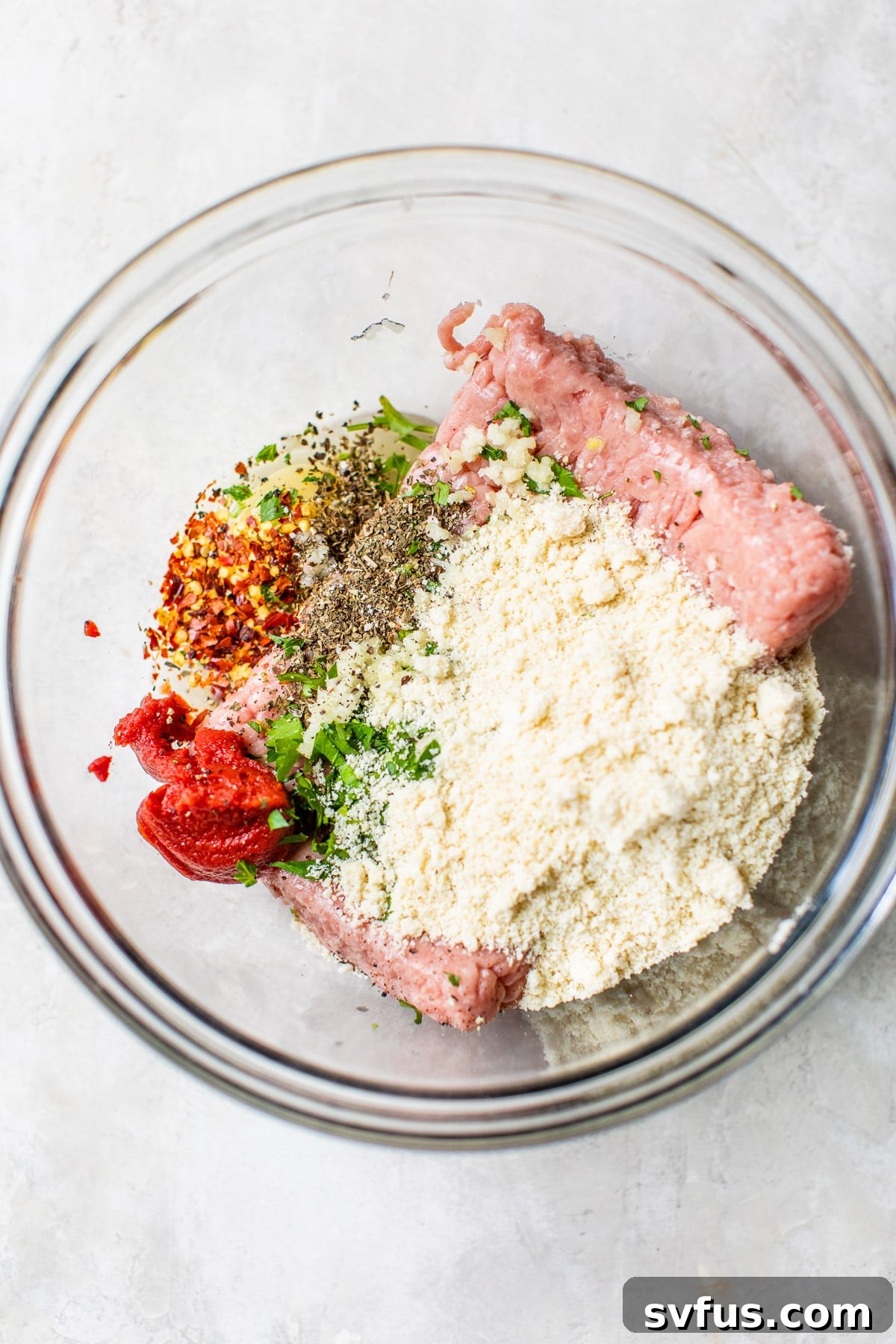 A bowl containing ground turkey, almond flour, and various spices before mixing, illustrating the initial step of combining ingredients.