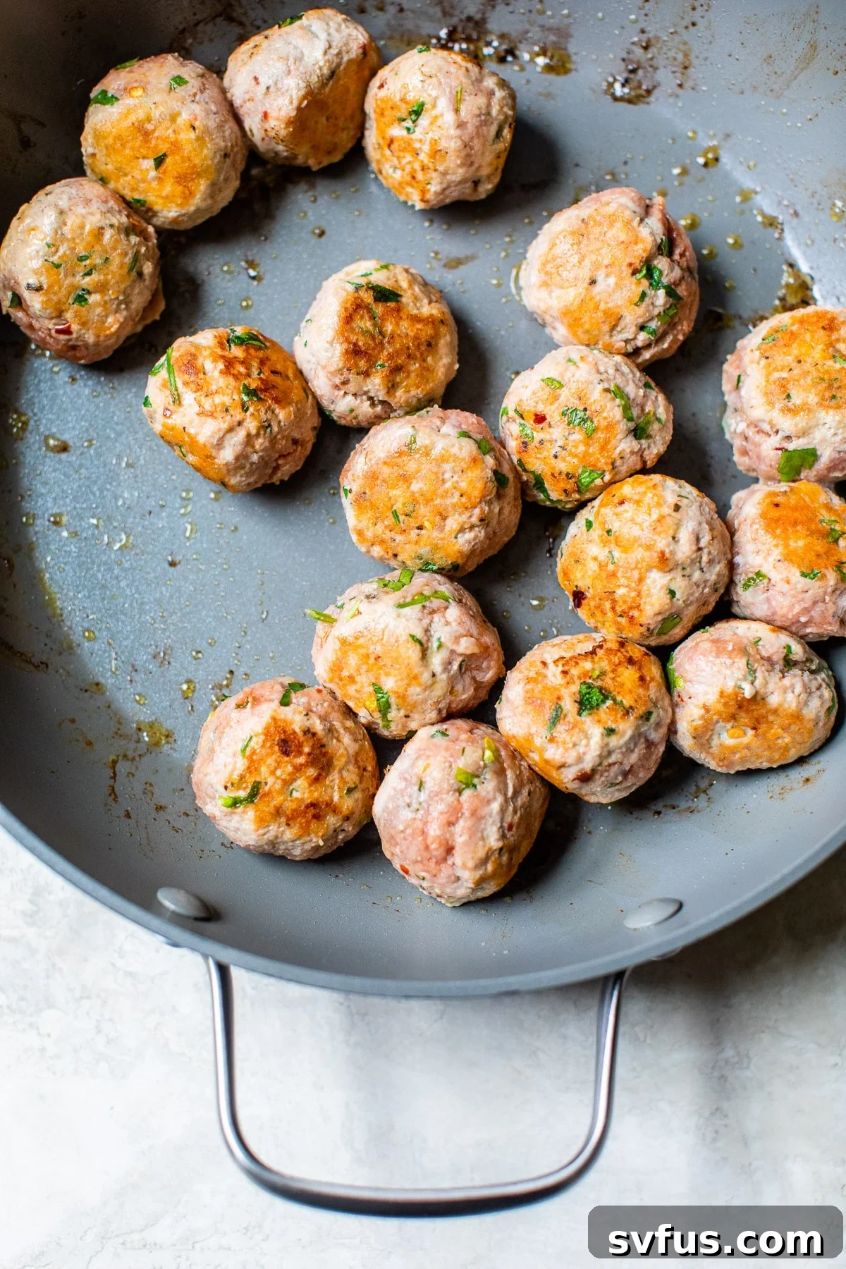 Partially seared paleo turkey meatballs in a hot skillet, with a golden-brown crust forming on their exterior.