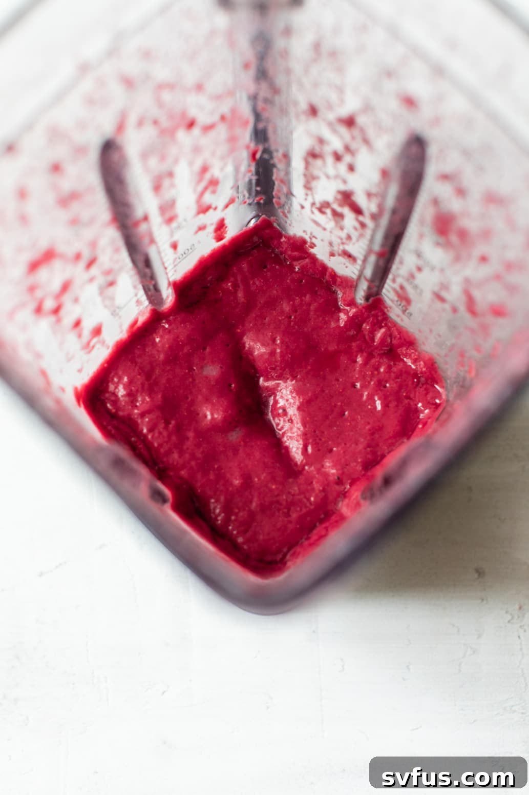 blended raspberries in a blender, forming the first layer of the raspberry orange smoothie