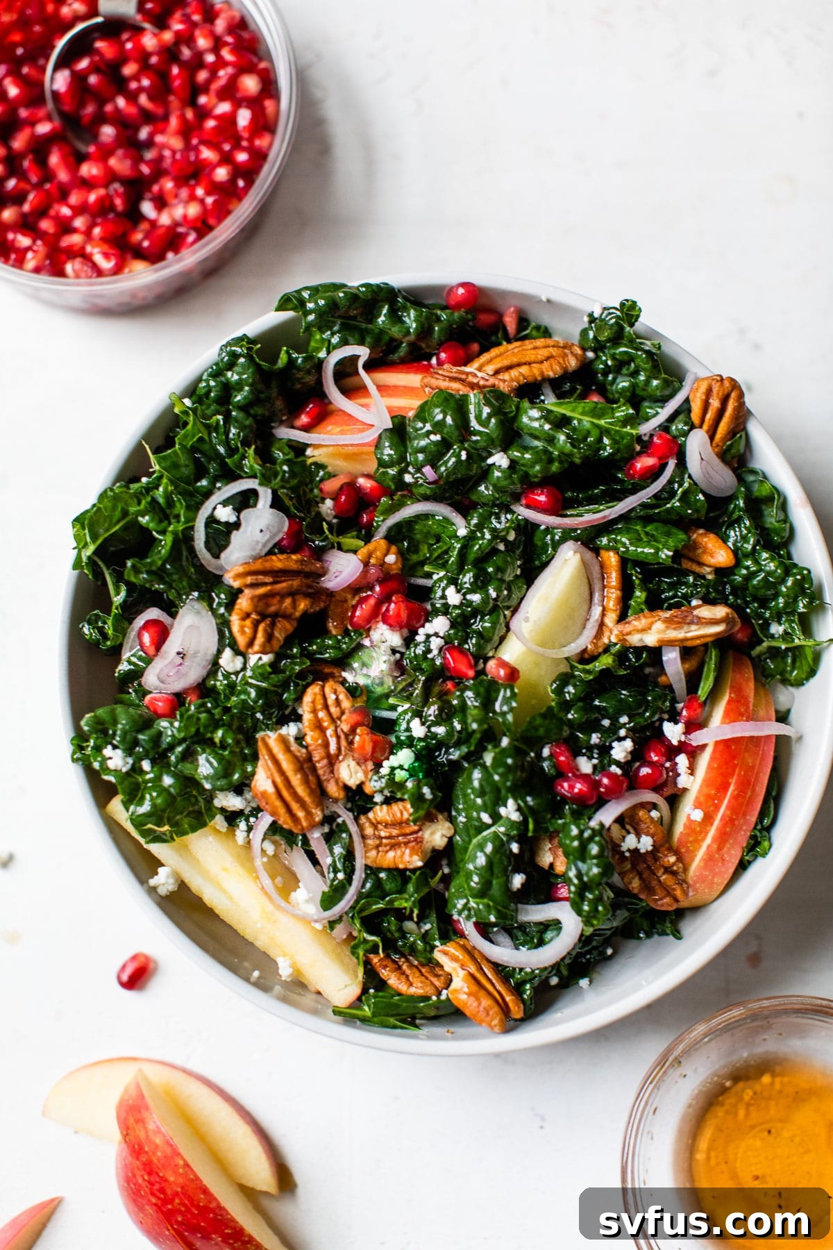 A close-up shot of the finished winter kale salad, garnished with additional apple, shallot, and pomegranate seeds, showcasing its fresh and inviting appearance.
