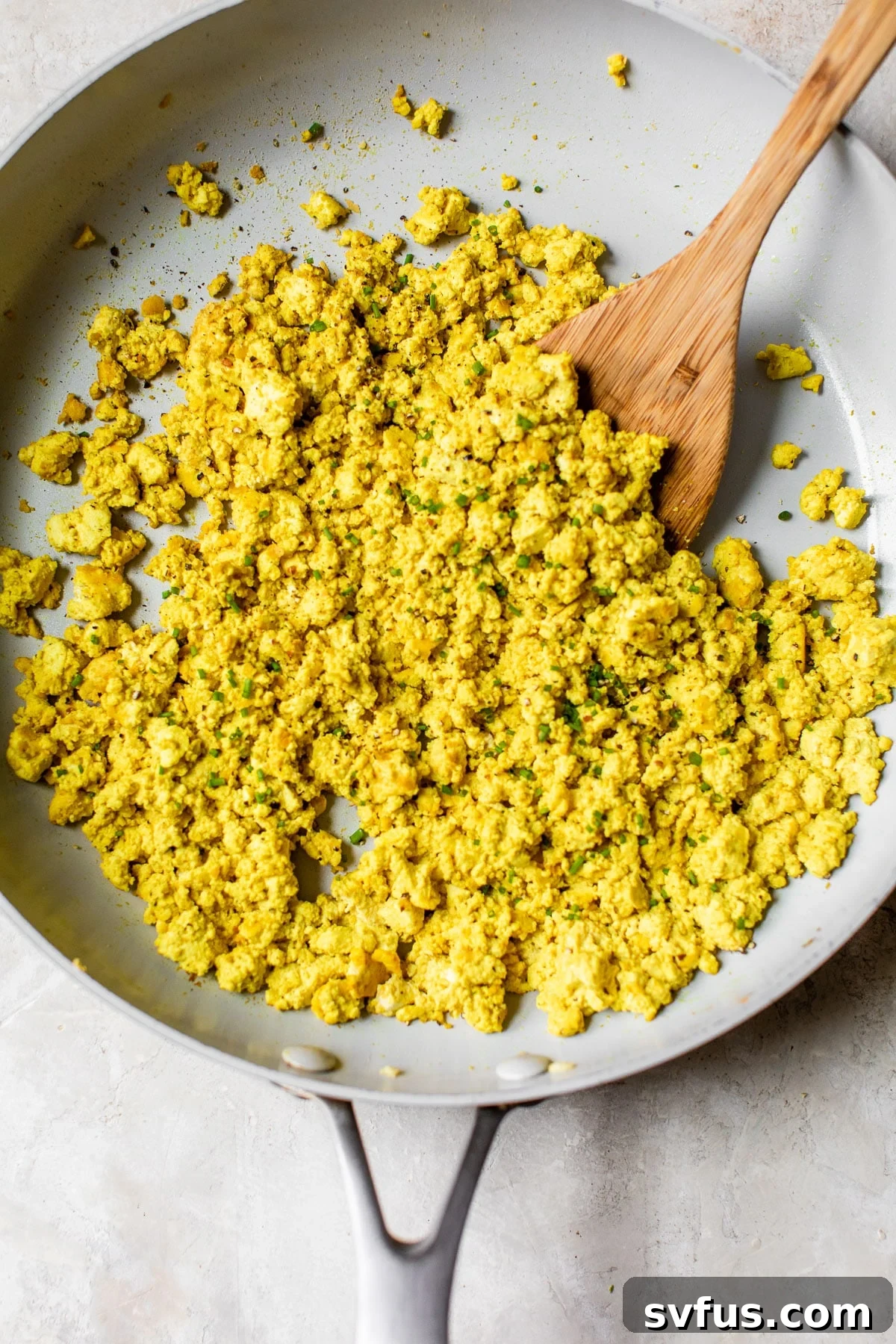Flavorful faux eggs topped with fresh chopped chives, served hot in a rustic skillet, ready to be enjoyed as a hearty plant-based breakfast.