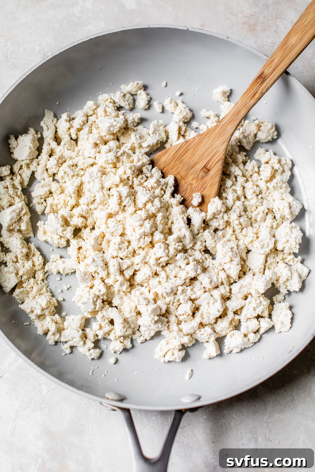 Tofu pieces expertly broken up and beginning to sauté in a skillet, taking on the desired texture for a perfect scramble.
