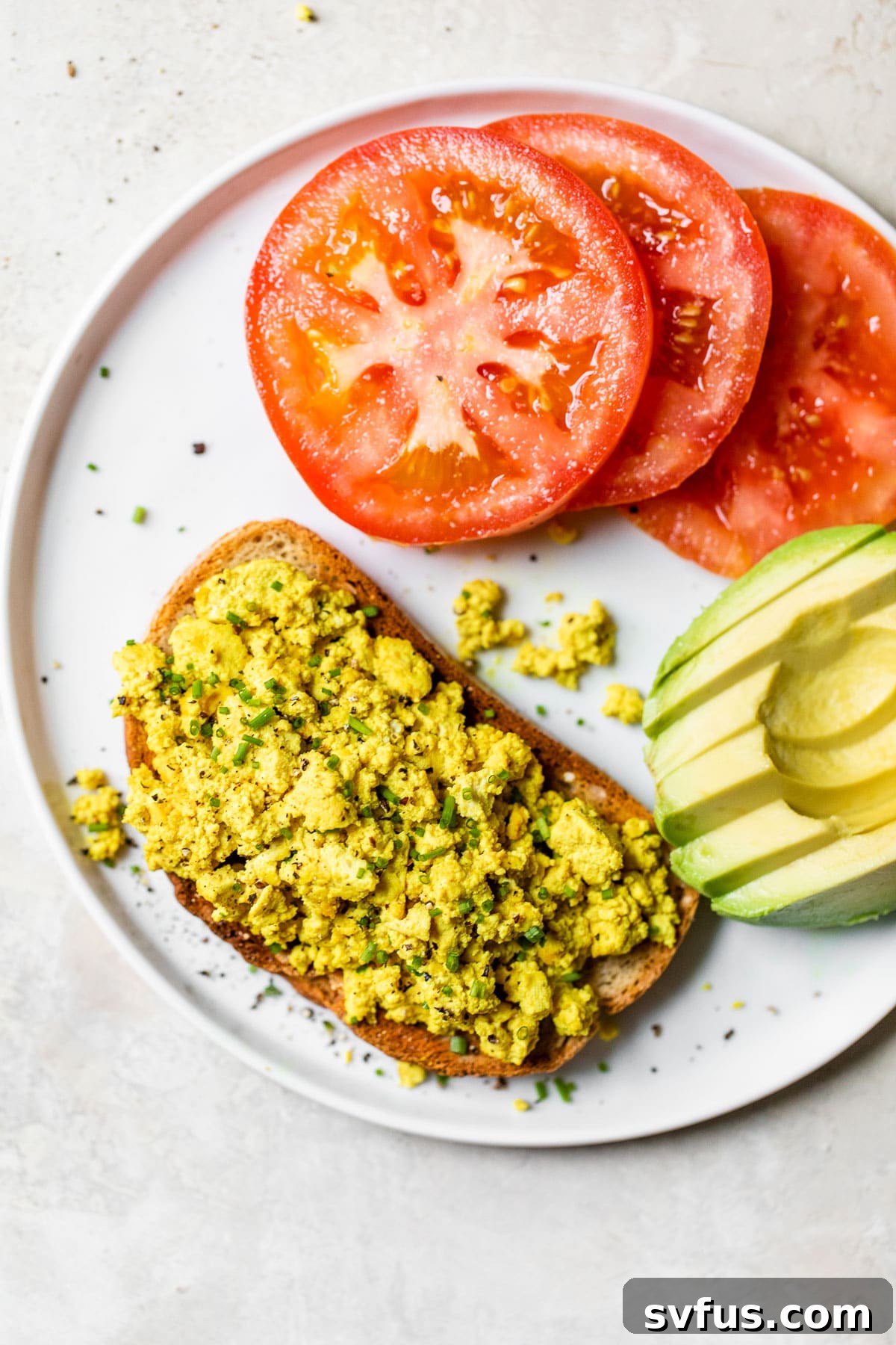 A beautifully plated tofu scramble on golden toast, flanked by fresh avocado slices and vibrant cherry tomatoes, creating a complete and balanced vegan breakfast.