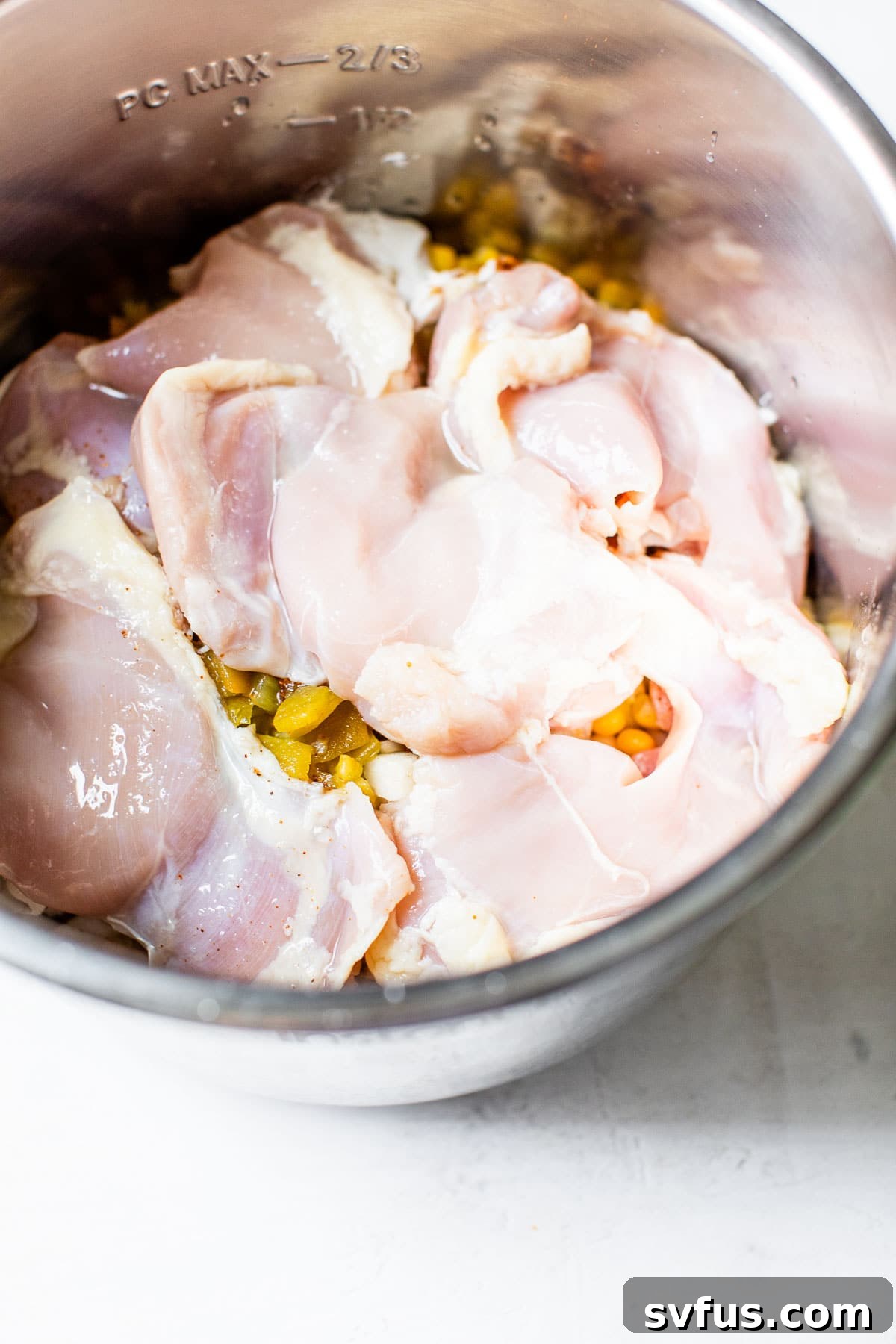 The Instant Pot filled with layers of ingredients: beans, corn, onions, garlic, green chiles, spices, and chicken thighs, ready for cooking.