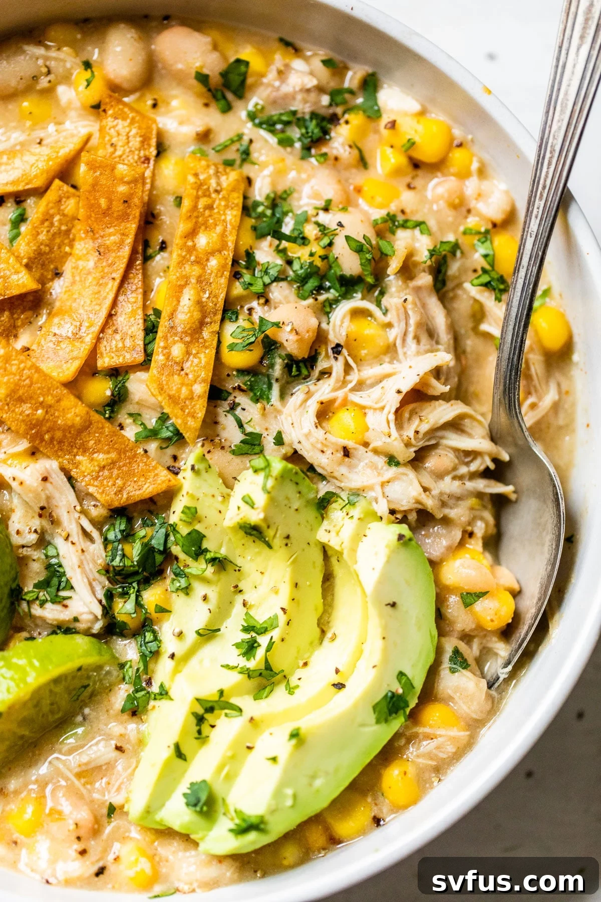 A close-up view of a bowl of Instant Pot White Chicken Chili, generously topped with shredded chicken, slices of fresh avocado, and crispy tortilla strips, ready for serving.