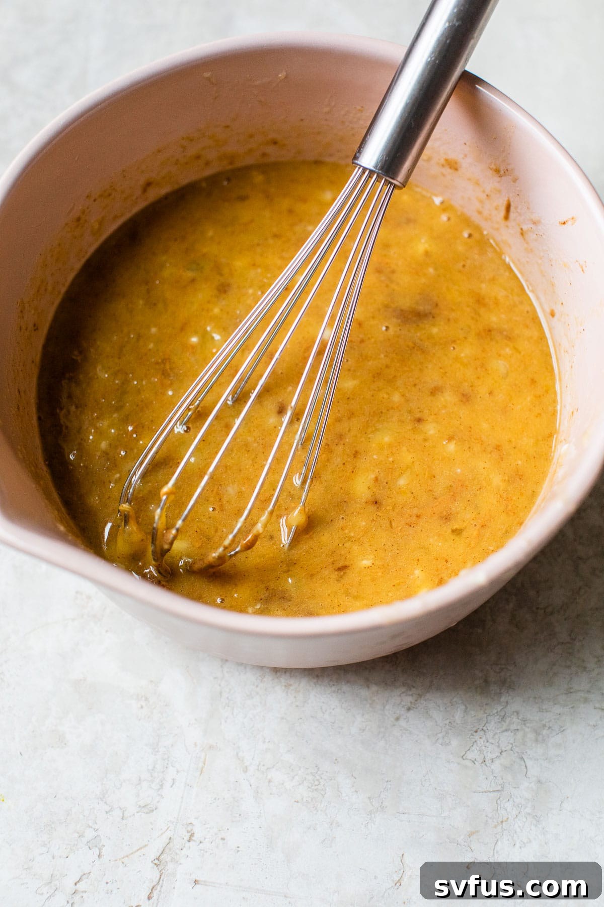 Whisked wet ingredients in a mixing bowl, featuring mashed bananas, eggs, almond butter, syrup, and vanilla.