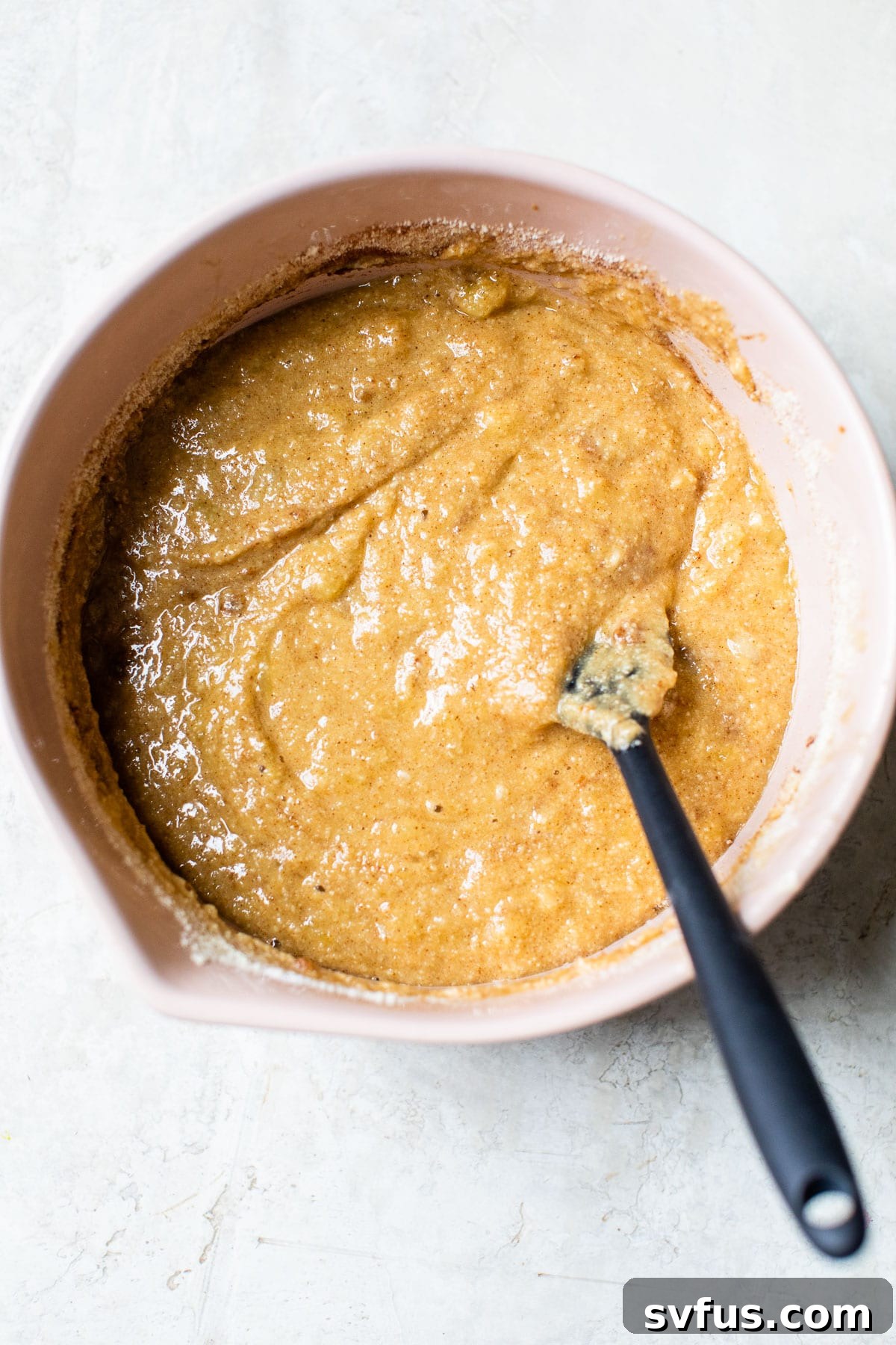 Muffin batter in a pink mixing bowl with a spatula, showing the combined wet and dry ingredients.