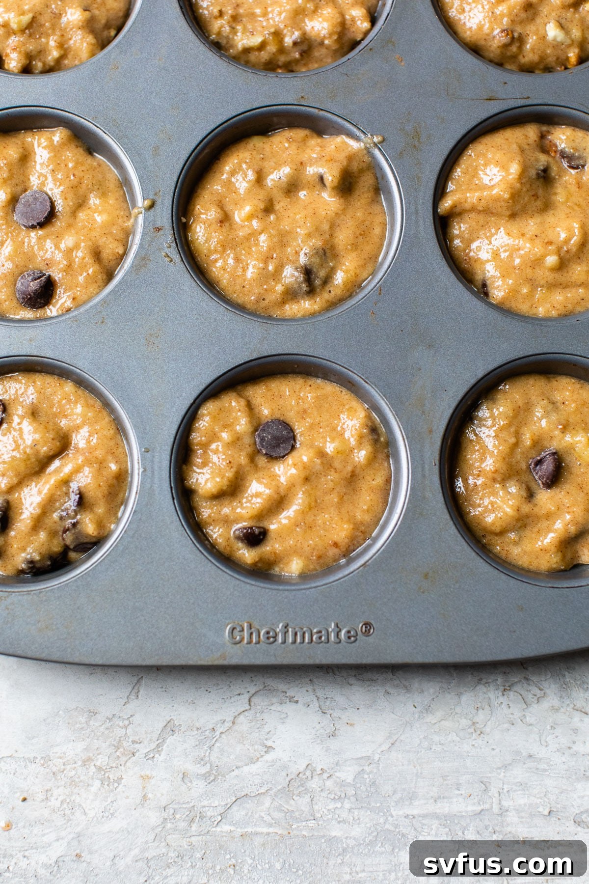 Muffin batter with chocolate chips evenly divided into a muffin tin, ready for baking.
