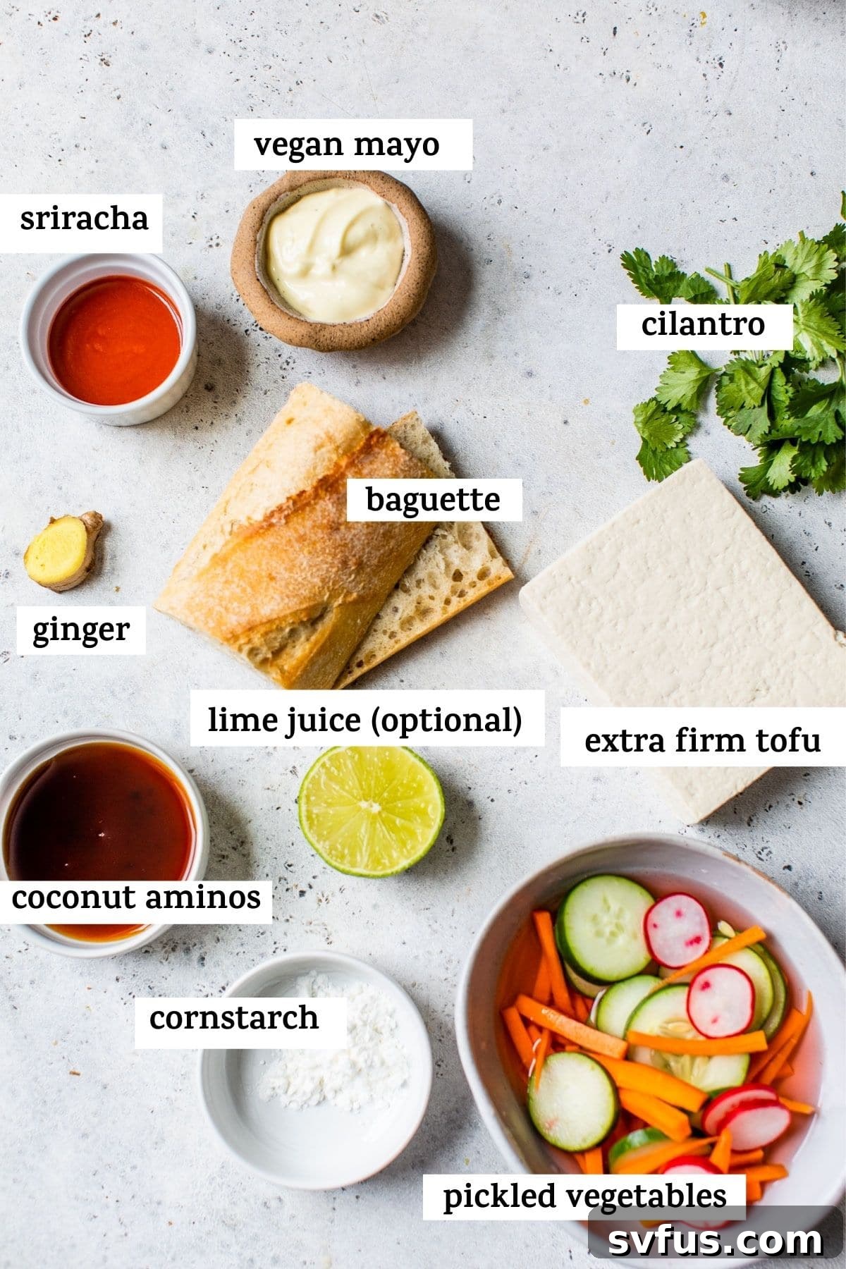 Arrangement of Tofu Banh Mi ingredients including sliced tofu, fresh herbs, pickled vegetables, and sauces, artfully presented on a kitchen counter.