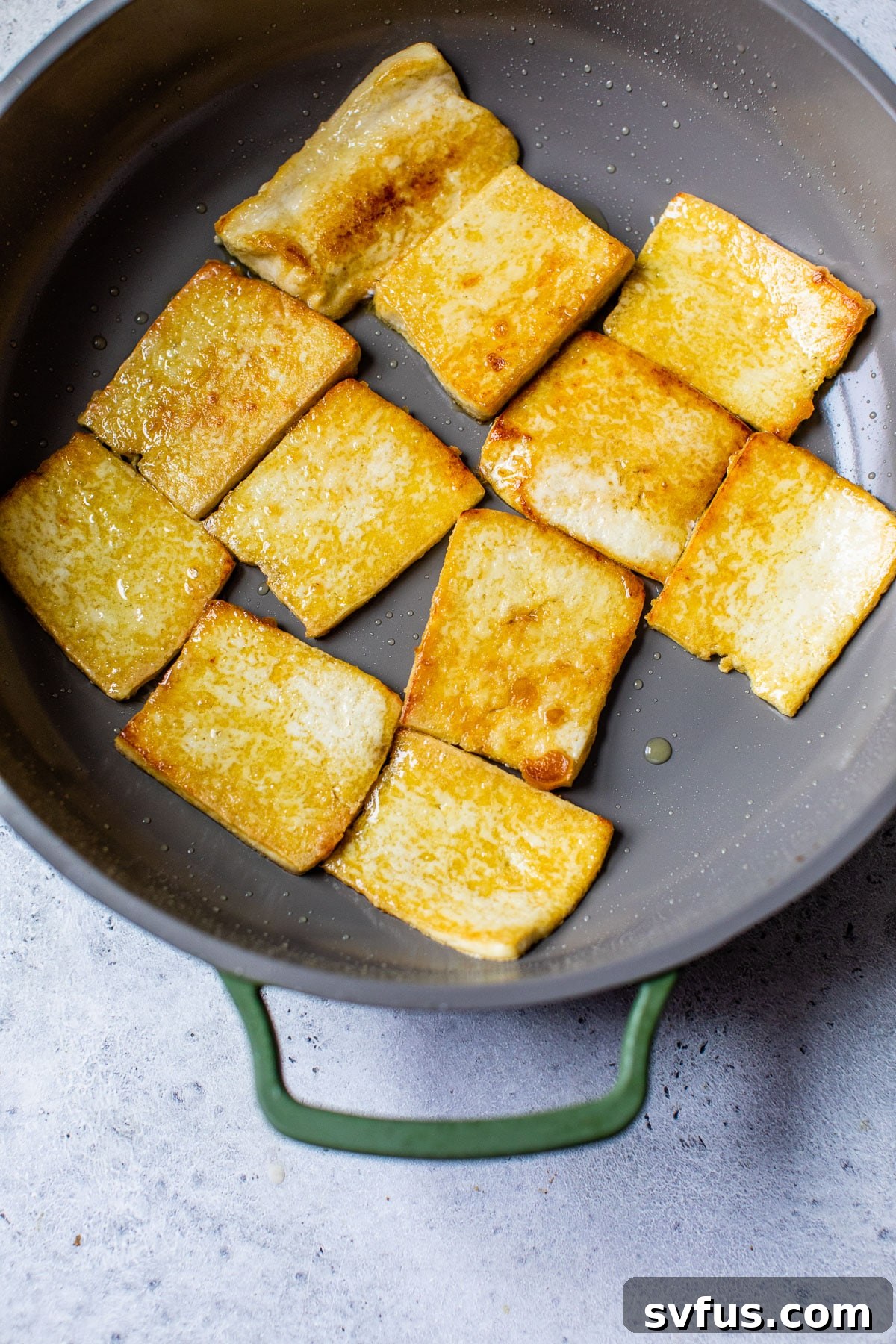 Pan-fried tofu sizzling in a nonstick skillet, achieving a golden-brown crisp, with visible oil around the edges.