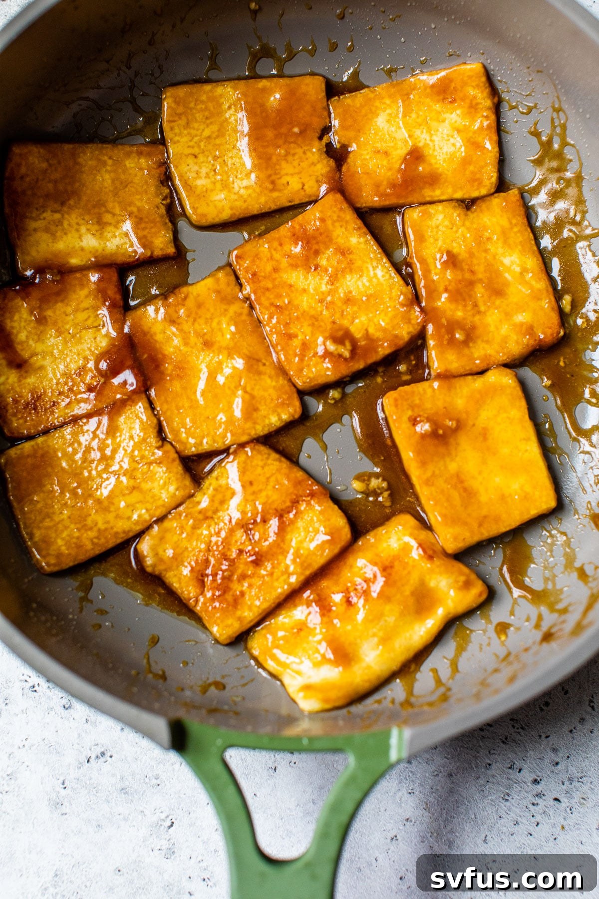 Cooked tofu slices in a skillet, now coated in a glossy, rich sauce, absorbing the marinade after frying.