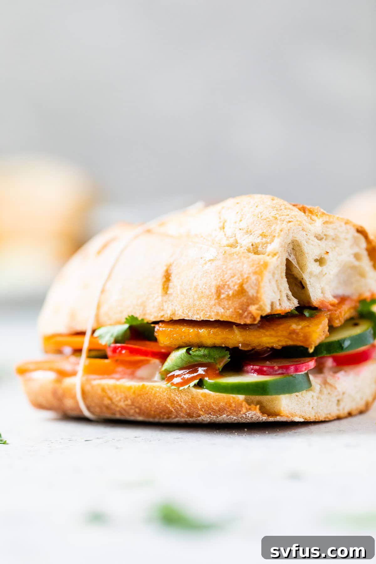 A freshly assembled Tofu Banh Mi sandwich, garnished with cilantro, placed on a light-colored table, invitingly ready to be enjoyed.