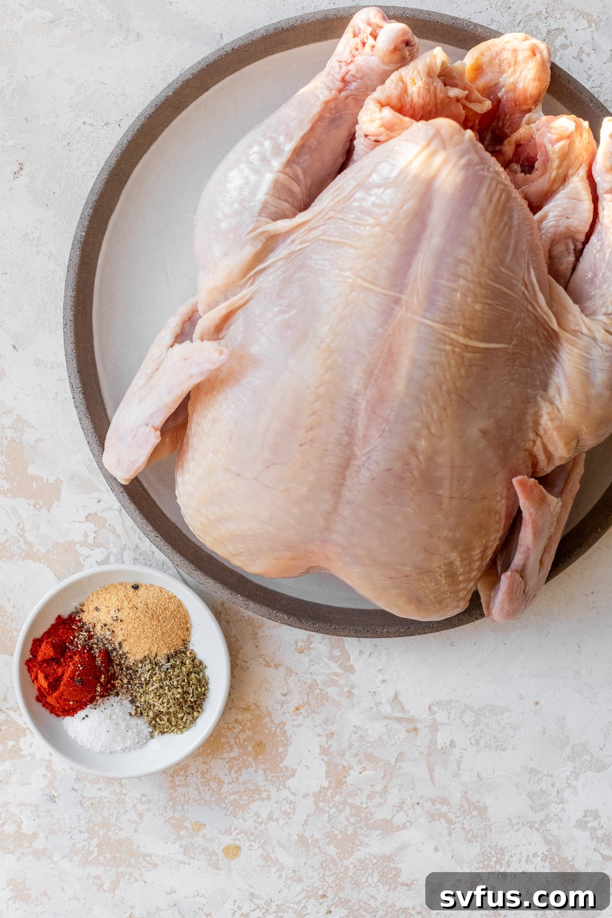 whole chicken on a plate with spices in a small dish off to the side