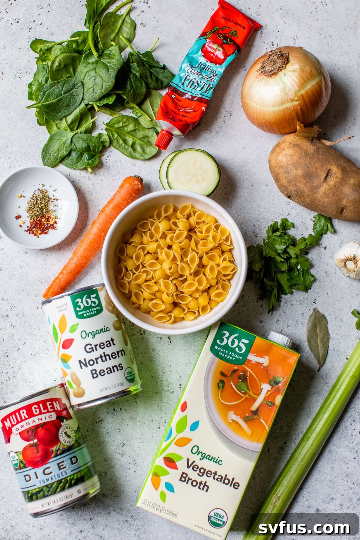 A colorful array of fresh minestrone soup ingredients laid out on a kitchen counter: potatoes, zucchini, canned tomatoes, beans, pasta, and herbs, ready for preparation.