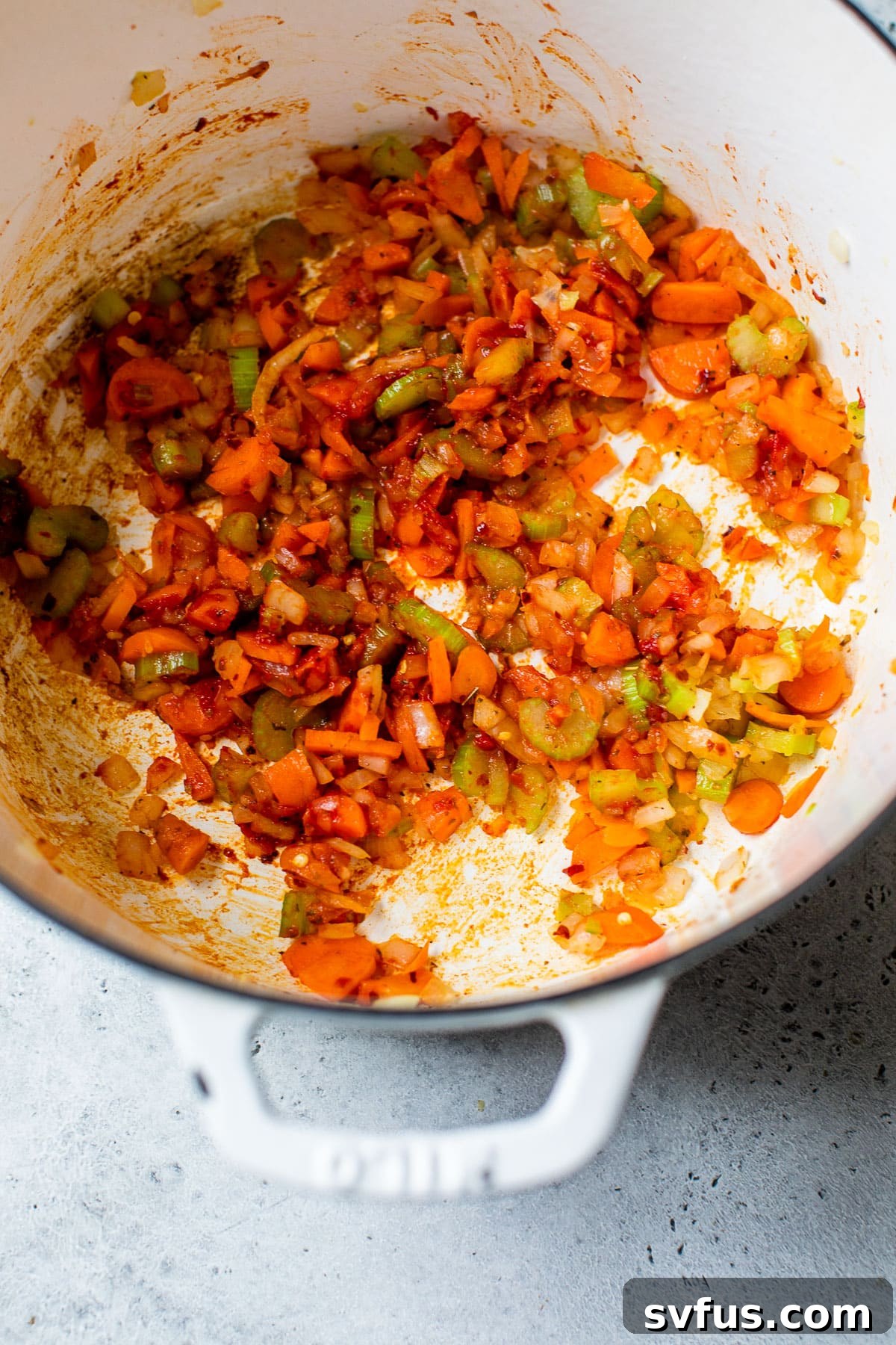 A close-up view of sautéed carrots, celery, and onions with garlic and spices mingling in a Dutch oven, creating an aromatic base for the minestrone.