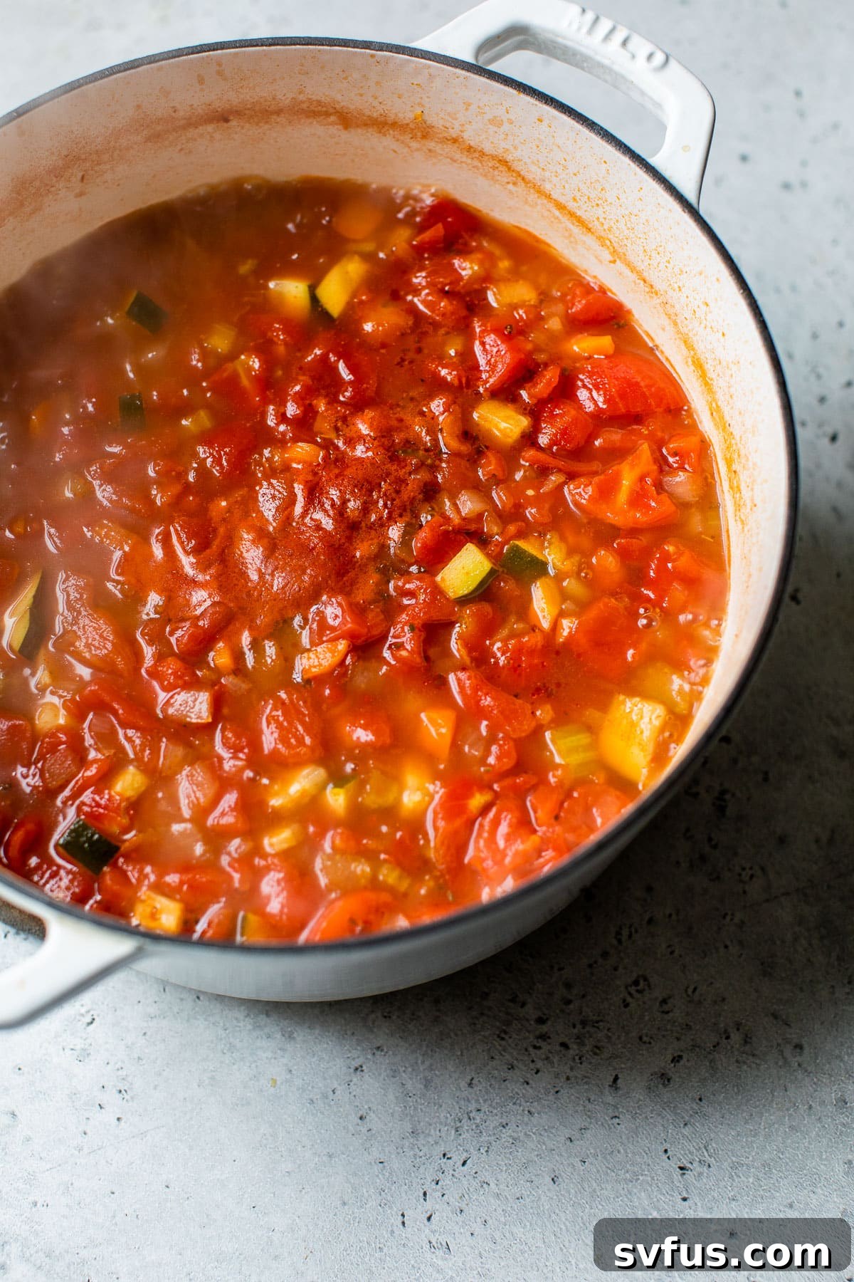 A vibrant tomato-based soup, brimming with diced vegetables, simmering gently in a large Dutch oven, promising warmth and flavor.