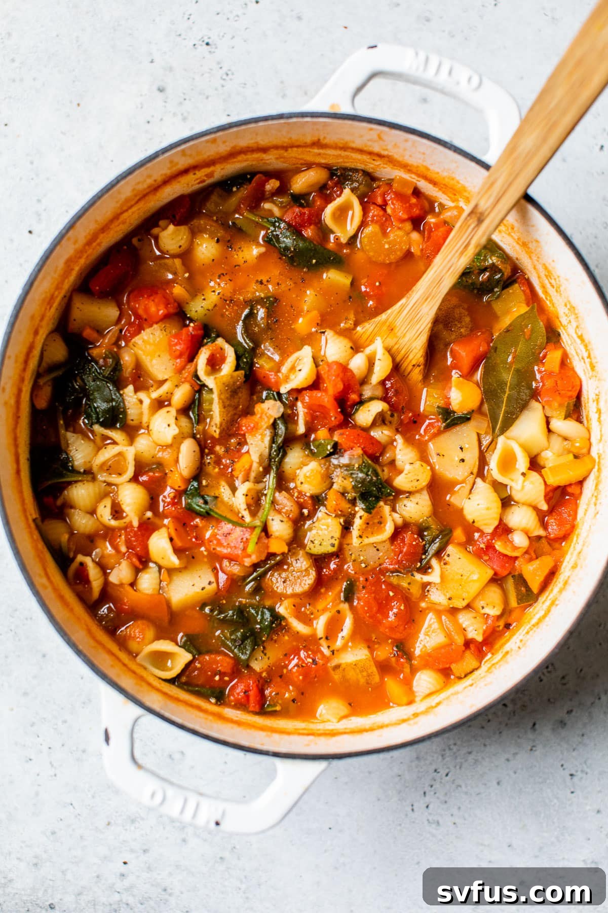 A hearty vegan minestrone soup, perfectly cooked with tender pasta, beans, and fresh spinach, ready to be served from a large Dutch oven.