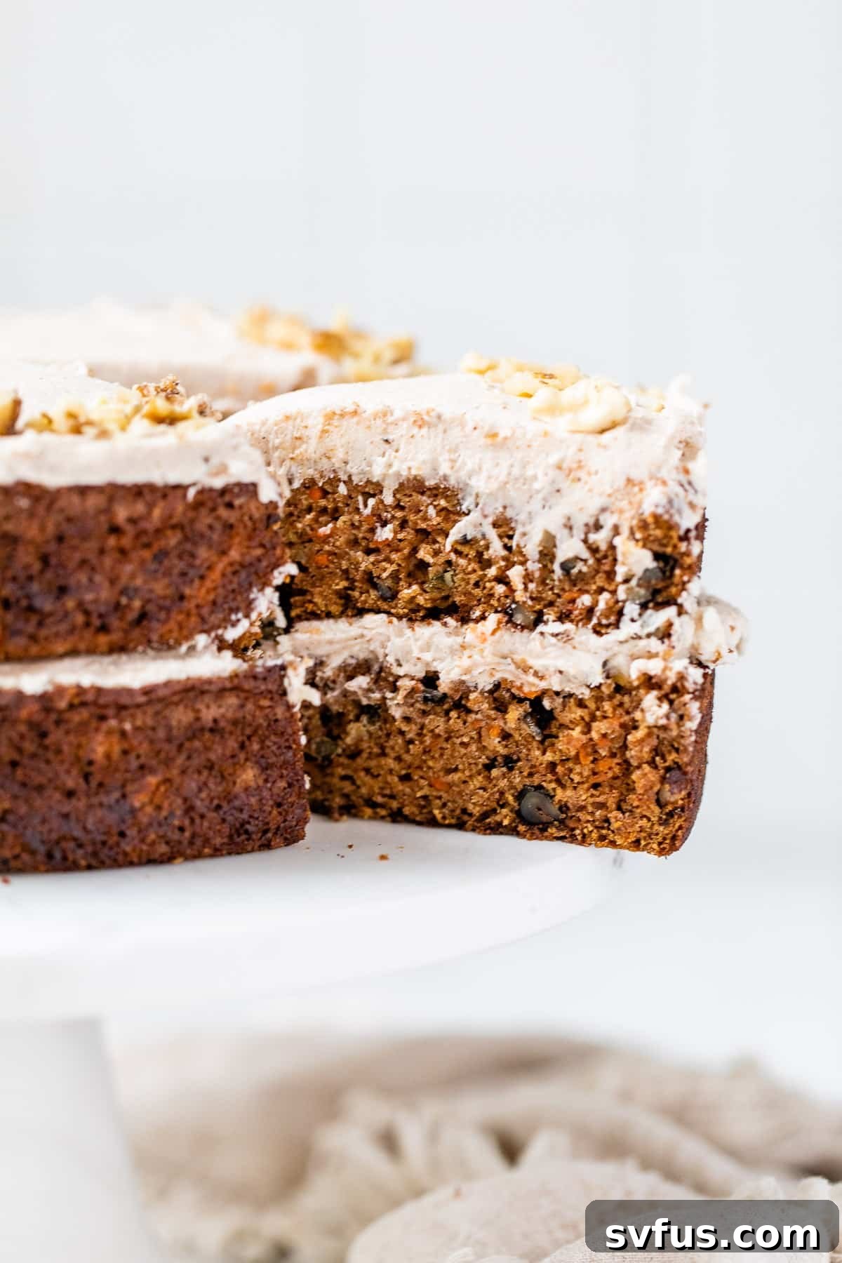 A beautifully decorated two-layer vegan carrot cake on a cake stand, with one slice elegantly removed to reveal its moist interior and generous frosting.