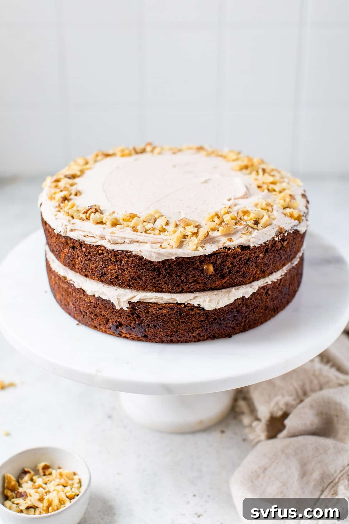 A two-layer vegan carrot cake, expertly frosted and presented on a cake stand, showcasing its inviting appearance.