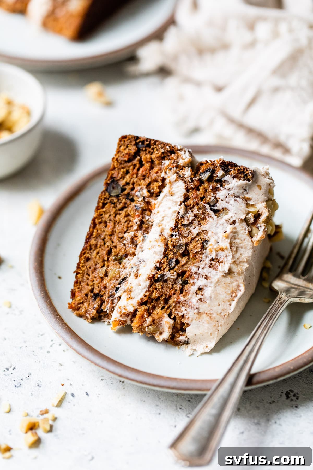 A perfectly sliced piece of vegan carrot cake on a white plate, highlighting its moist layers and creamy frosting.