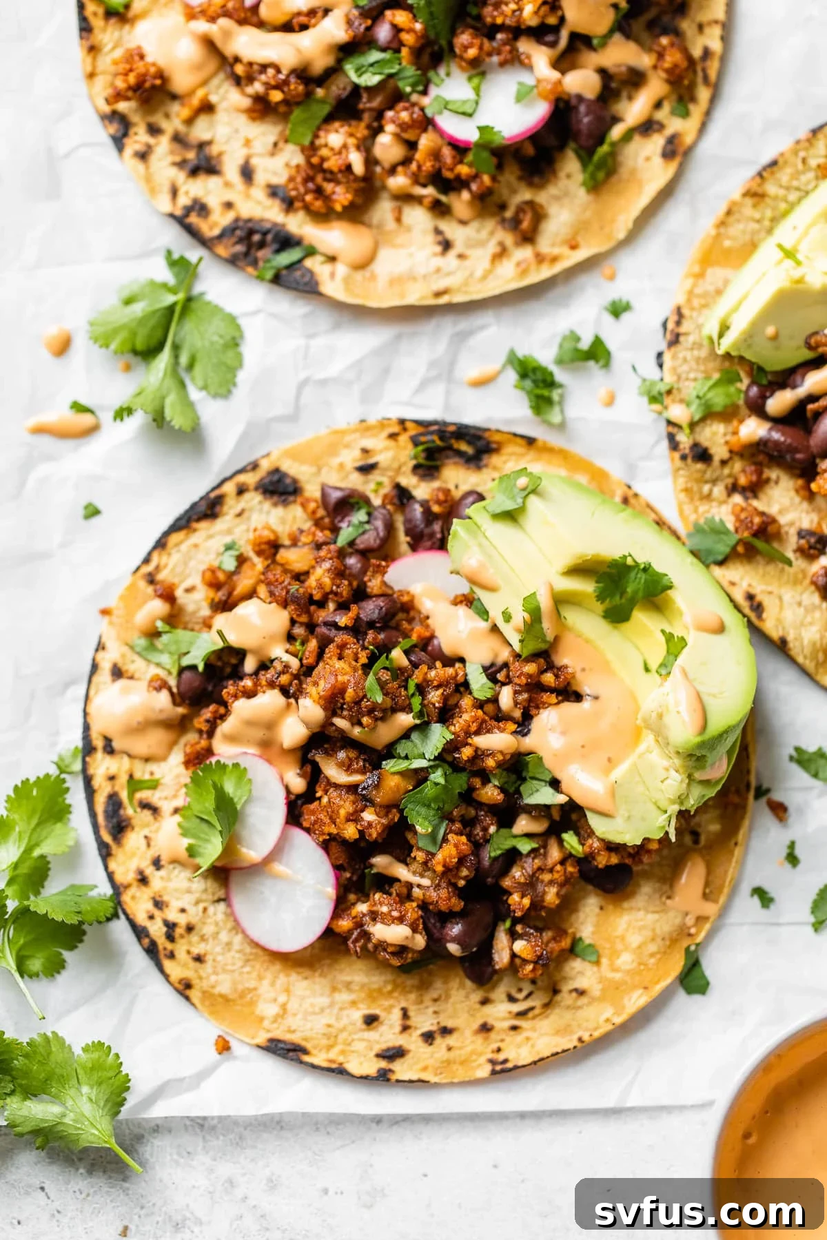Close-up of a vibrant vegan walnut taco on parchment paper, garnished with fresh cilantro, showcasing its rich texture and colorful toppings.