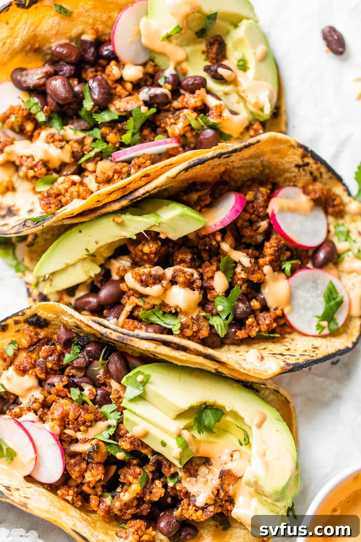 Three beautifully assembled vegan walnut tacos lined up on parchment paper, ready to be enjoyed, showing off their colorful toppings.