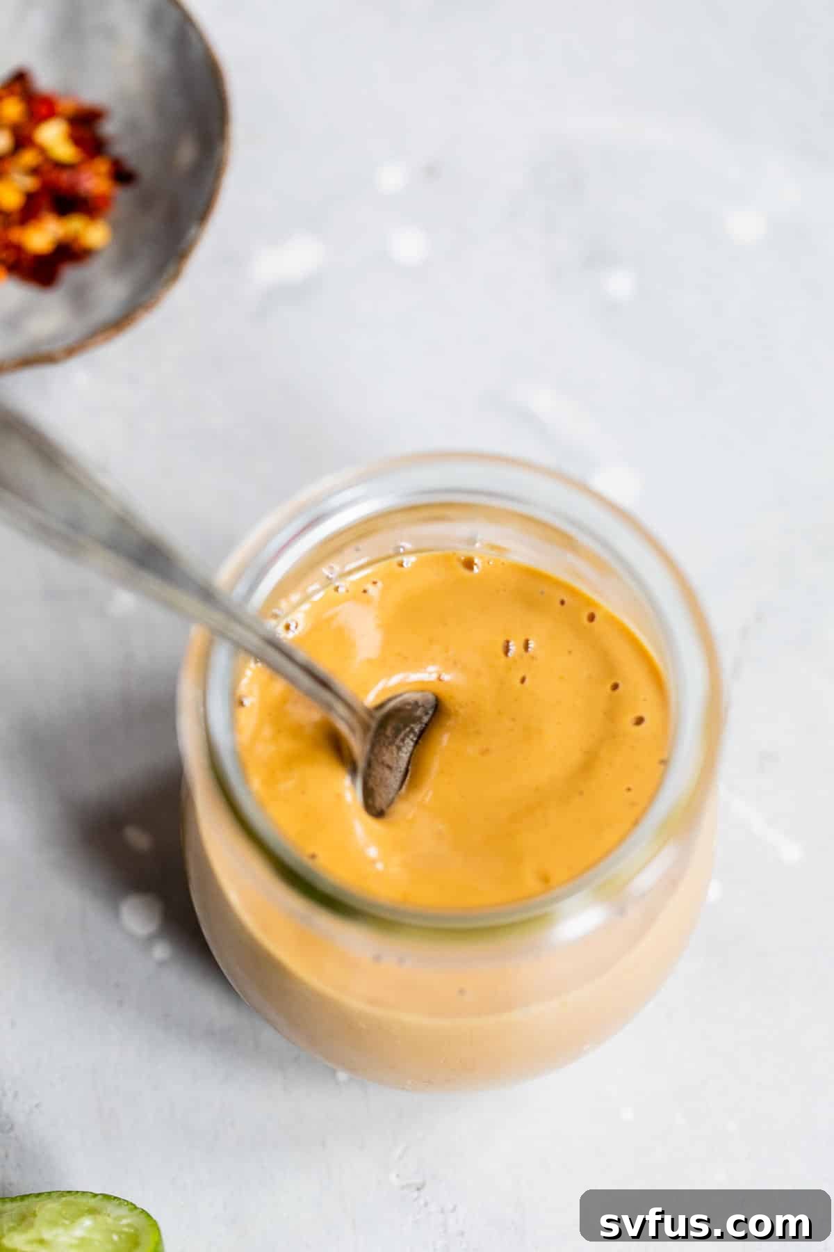 Close-up of vibrant orange peanut sauce in a glass jar with a small spoon, ready for serving