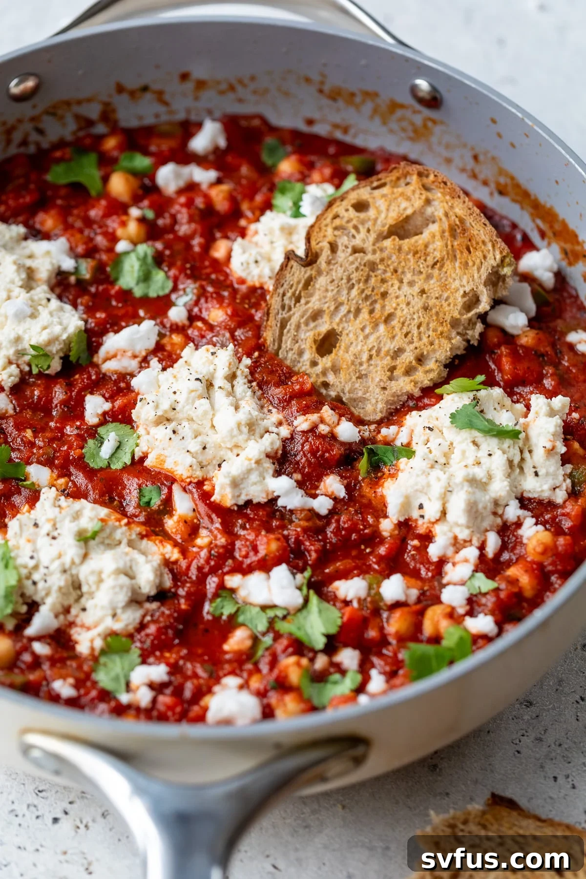 Vibrant Vegan Shakshuka in a cast iron skillet, garnished with fresh cilantro and creamy vegan ricotta, ready to be served with crusty bread for a delicious brunch
