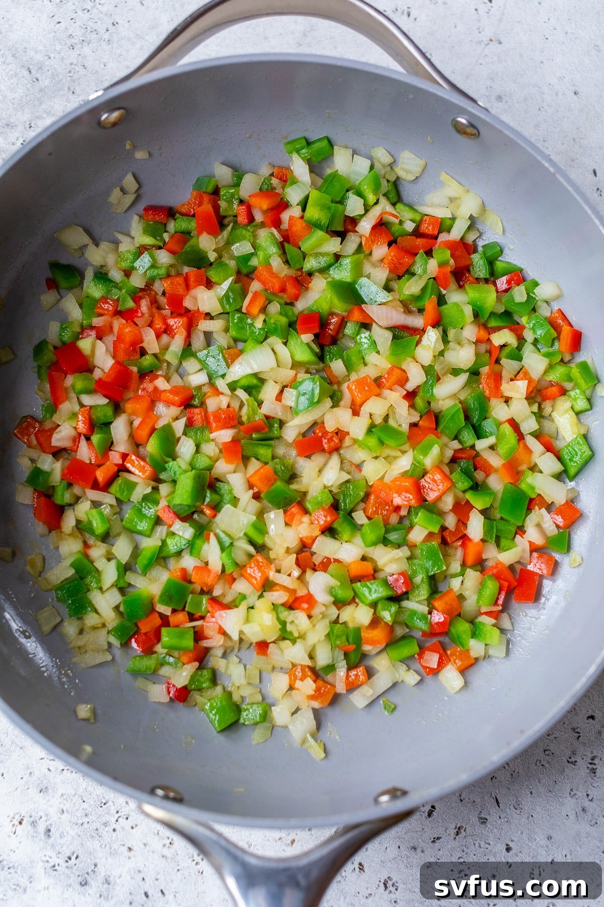 Sautéing finely diced onion, garlic, and colorful bell peppers in olive oil in a large skillet, creating an aromatic base for the vegan shakshuka