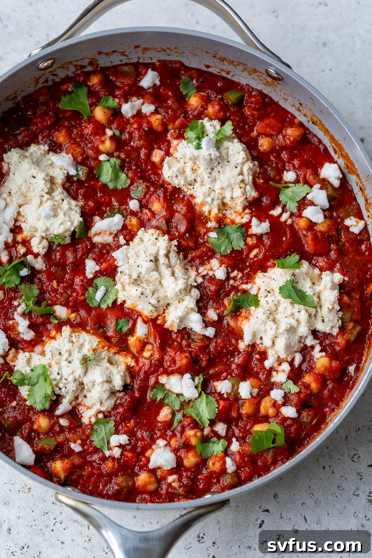 Overview of a freshly prepared vegan shakshuka in a skillet, beautifully topped with creamy vegan ricotta and fresh cilantro, ready for serving