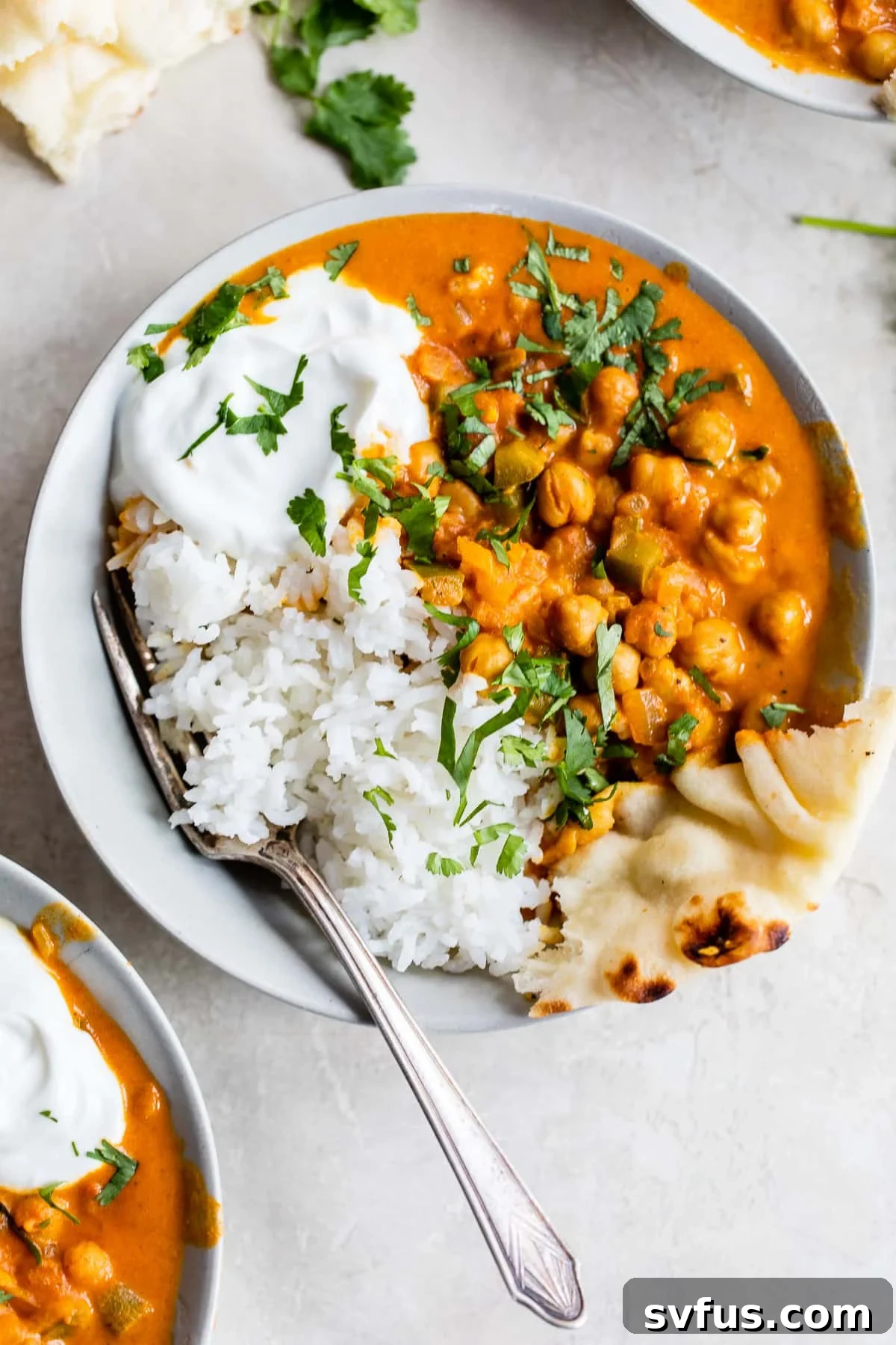 A vibrant bowl of vegan chickpea tikka masala, garnished with fresh cilantro, served alongside fluffy basmati rice and warm naan bread.