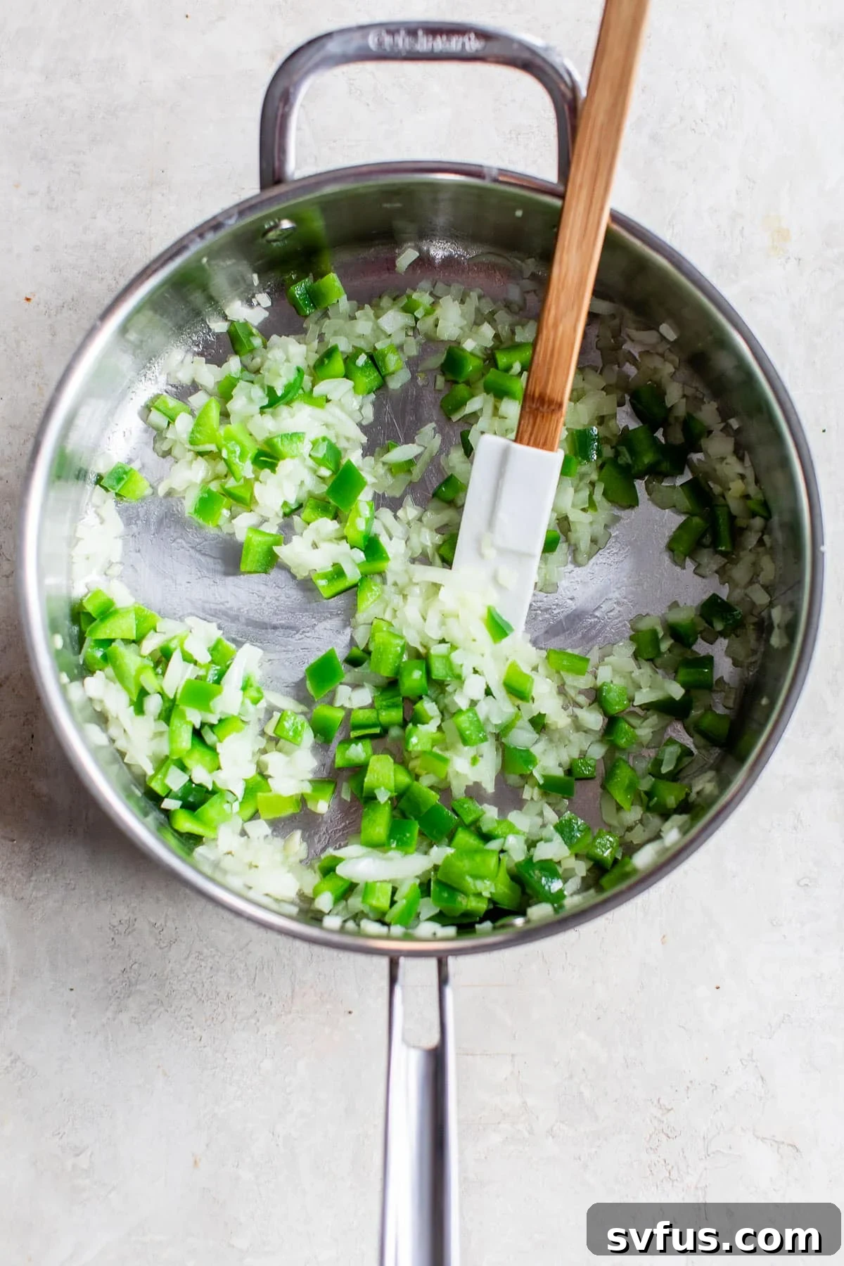 Diced green bell peppers and onions cooking in a skillet, gently softened and translucent.