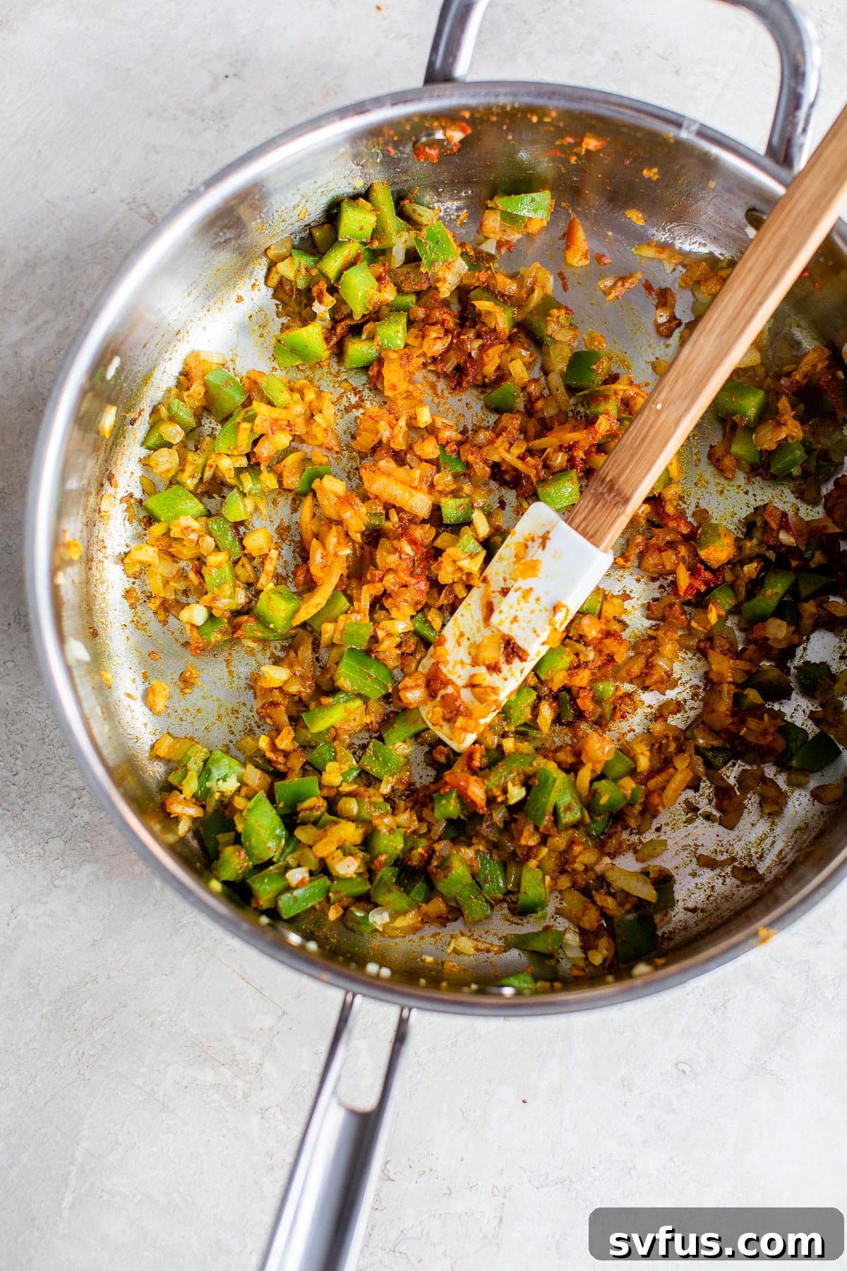 Finely diced peppers and onions coated in a vibrant mix of aromatic Indian spices, sautéing in a skillet.