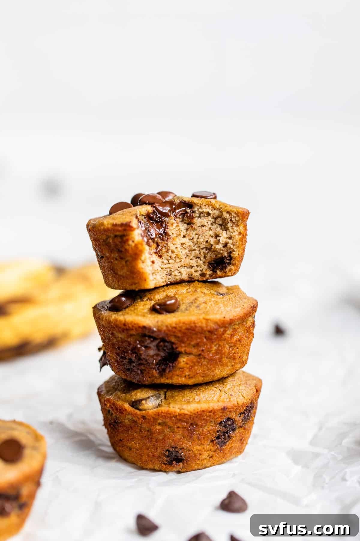 A perfectly stacked trio of golden-brown coconut flour banana muffins, generously studded with melted chocolate chips and a delicate crumb.