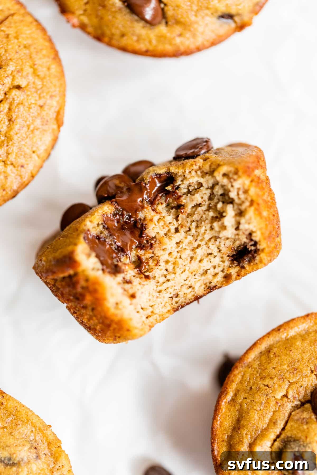 A single coconut flour banana muffin, with a bite taken out, showcasing its moist interior and chocolate chips, resting on parchment paper.