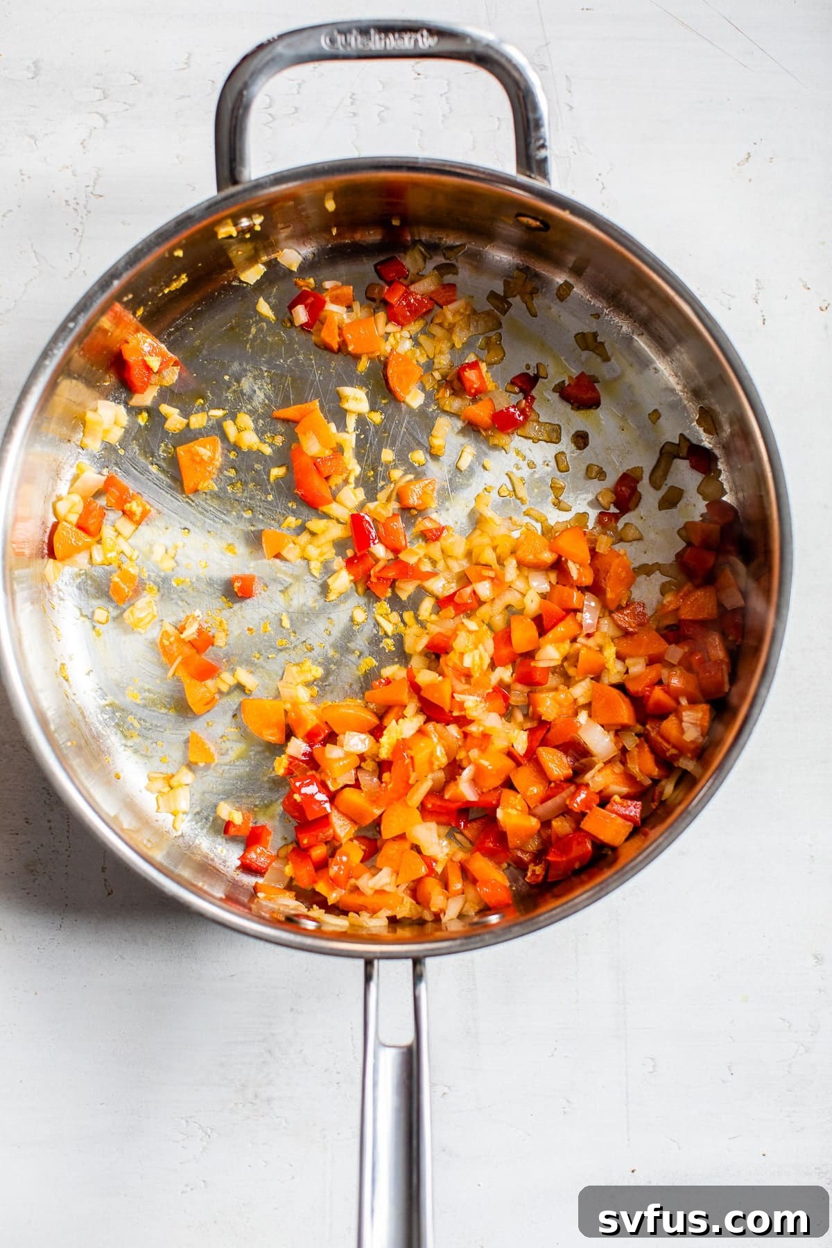Diced carrots and bell peppers gently cooking in olive oil in a large skillet, forming the base of the curry.