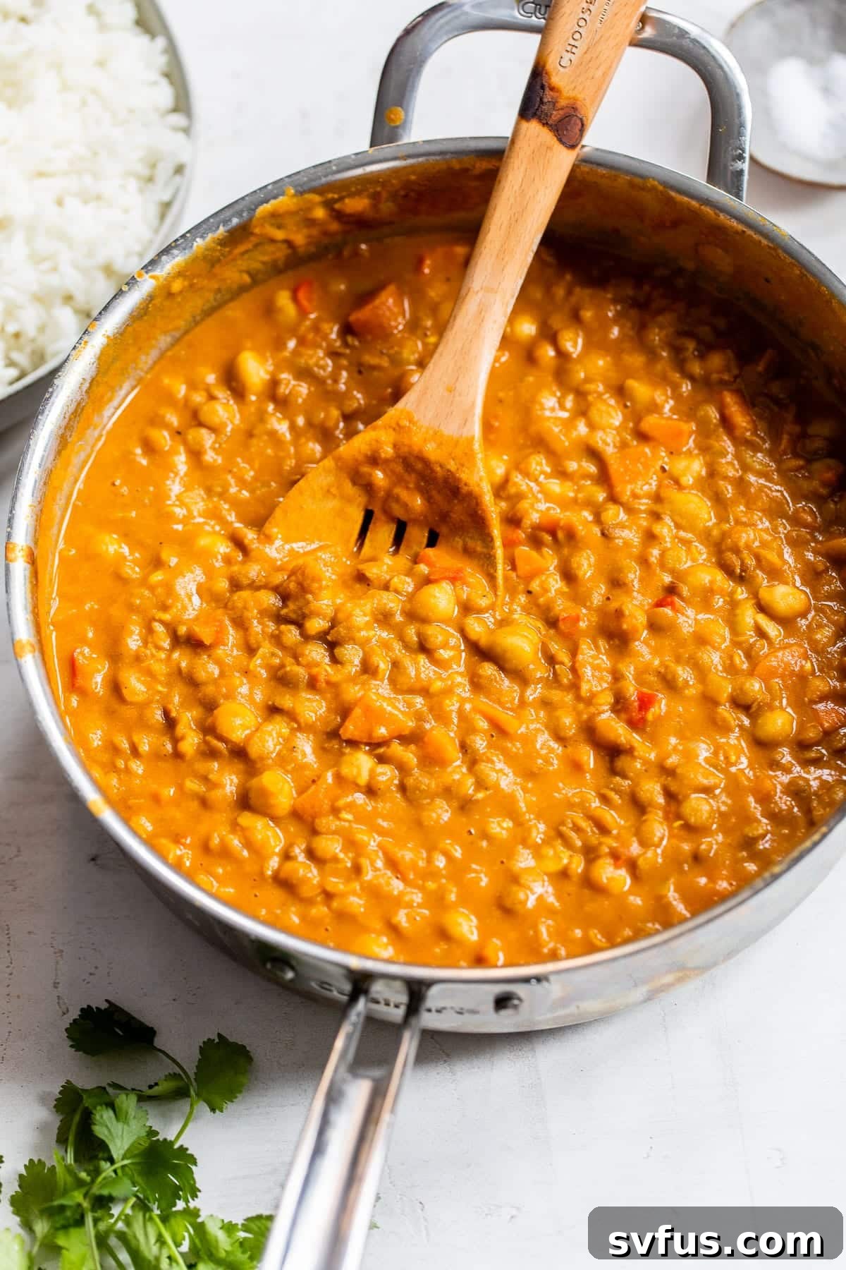 A close-up view of cooked chickpeas, lentils, and vegetables perfectly blended in a rich, orange curry sauce within a skillet.