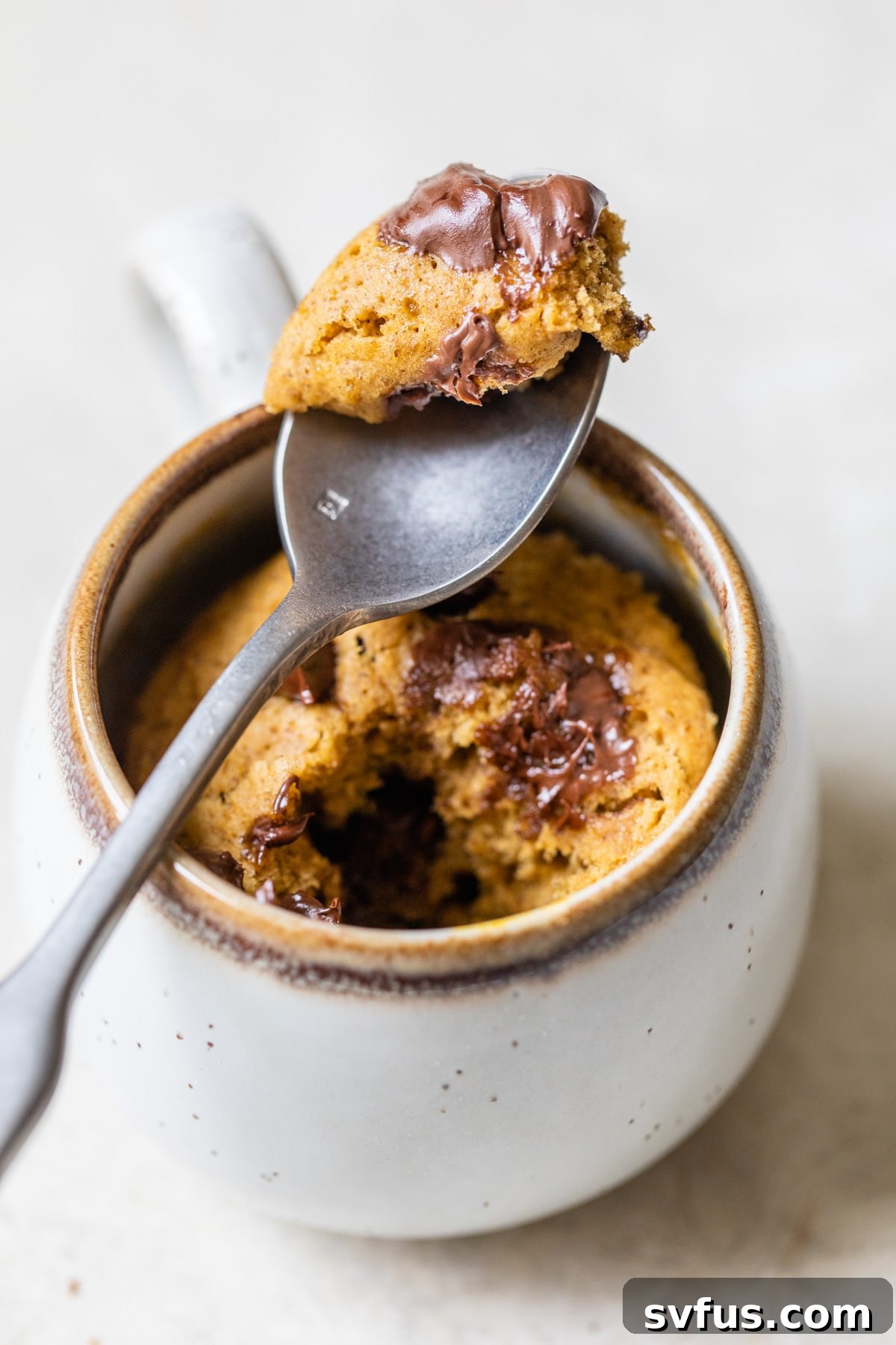 A close-up shot of a baked pumpkin mug cake, garnished with abundant melted chocolate chips and a dusting of powdered sugar, presented beautifully in a ceramic mug.