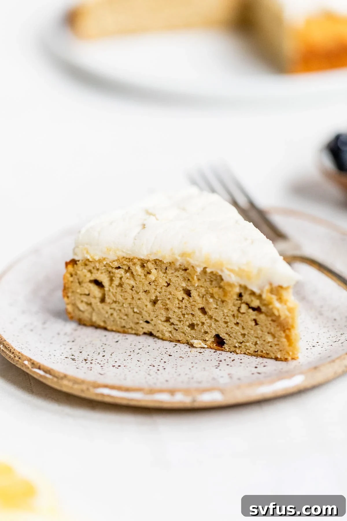 A beautifully sliced piece of moist Coconut Flour Cake, topped with a luscious vanilla icing, resting invitingly on a white plate, ready to be enjoyed.