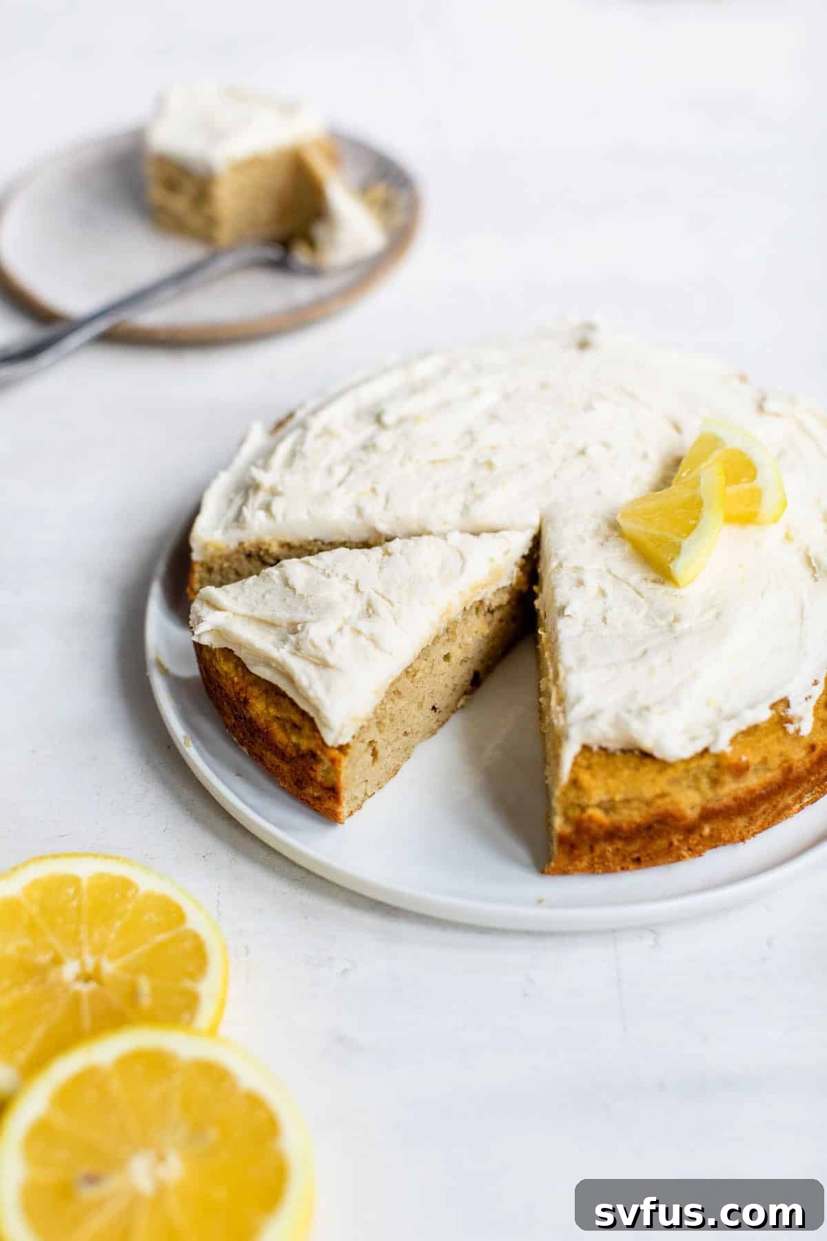 A beautiful, round Coconut Flour Cake presented on a plate, elegantly topped with a delicate layer of icing and garnished with fresh lemon wedges for a touch of zest.