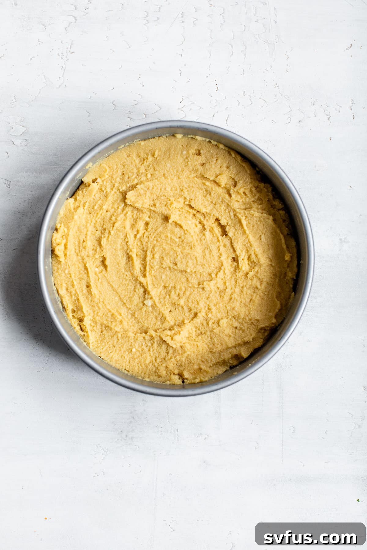 Smooth, light-colored cake batter evenly spread within a round cake pan, ready for baking in the oven.