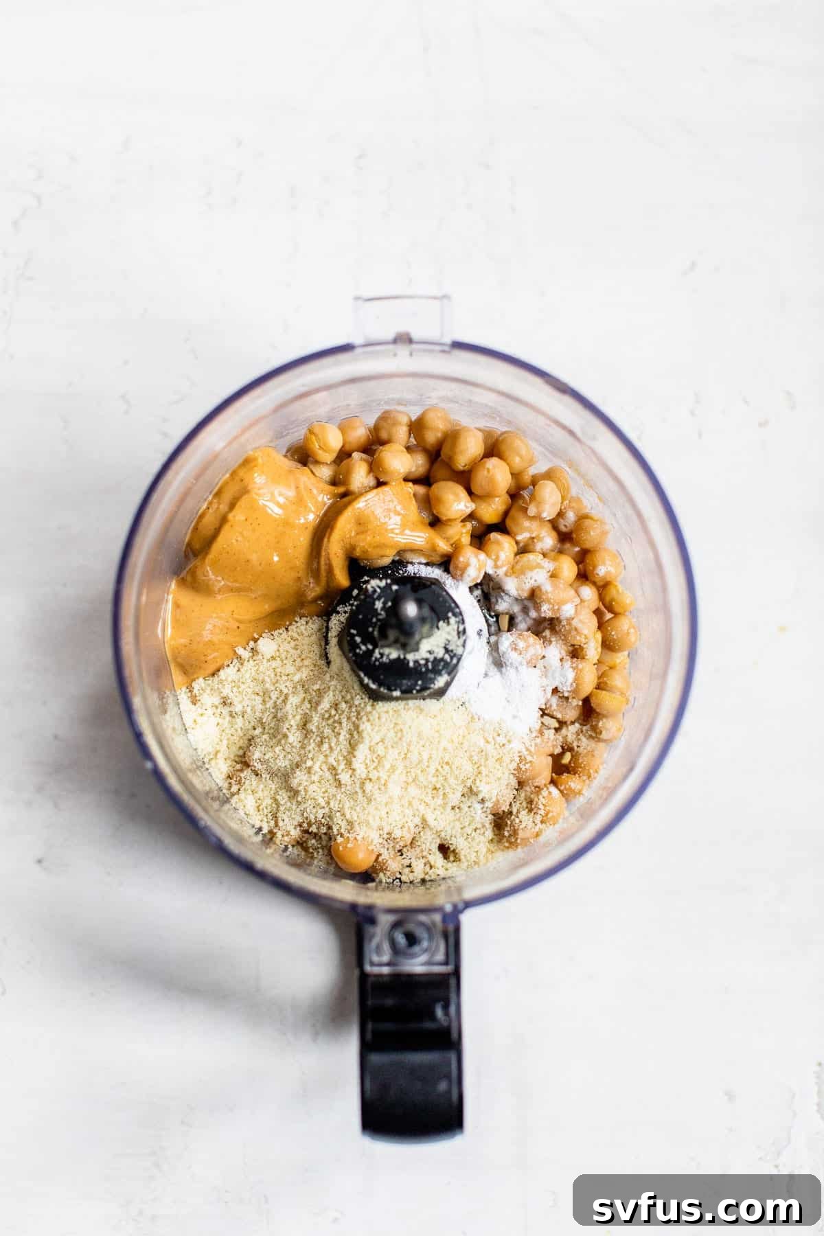 Chickpeas, peanut butter, and almond flour being pulsed in a food processor.