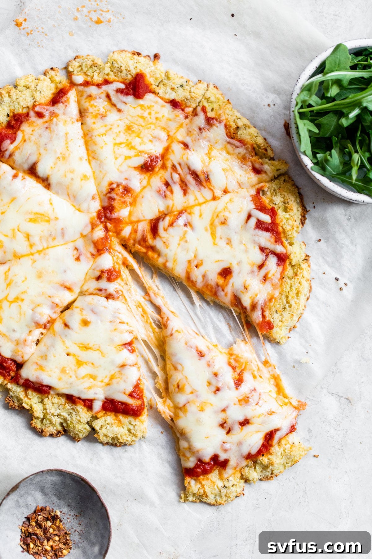 A slice of cauliflower crust pizza being gently lifted from the whole pizza, showcasing its sturdy yet delicious texture.