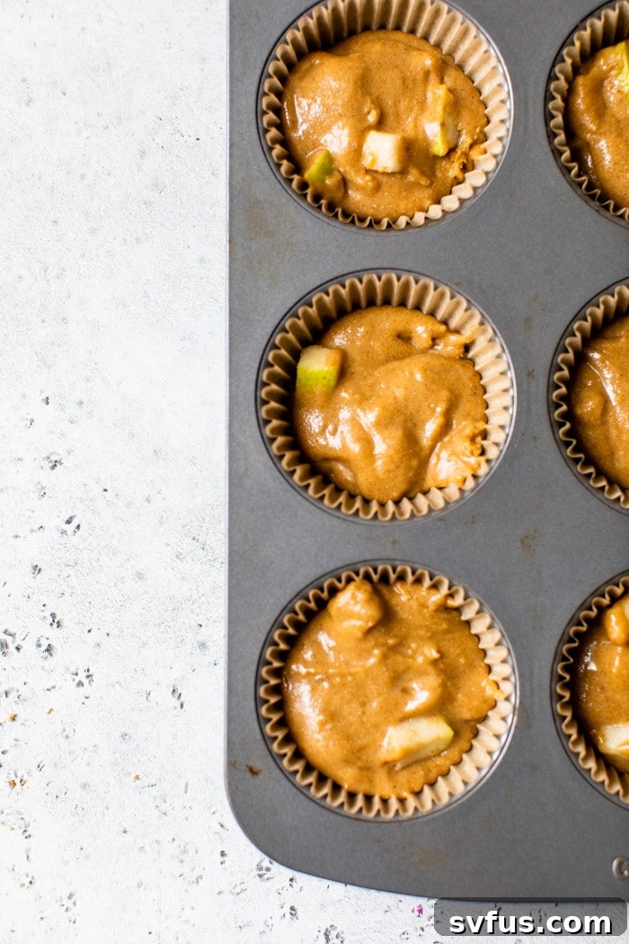Pear muffin batter filling a muffin tin, ready for baking.